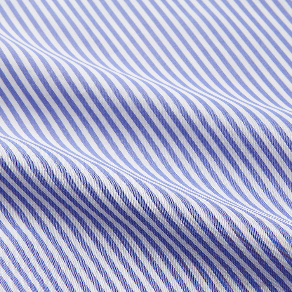 The Turnbull & Asser Blue Bengal Stripe Piped Cotton Nightshirt features long sleeves, a pointed collar, dark-trimmed pocket, curved hem, button details, and cuffed sleeves for an elegant look.