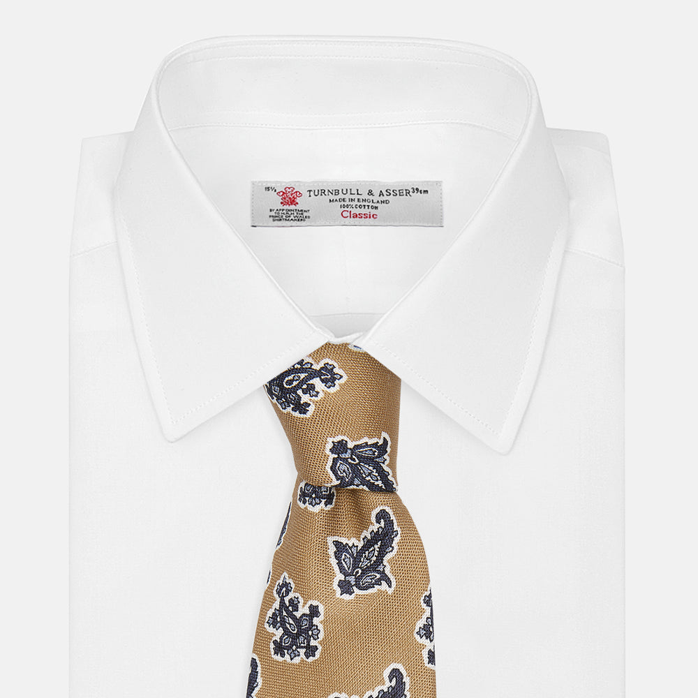 The Turnbull & Asser Toffee Paisley Floral Cotton Silk Blend Tie features a rolled-up design with dark blue and white paisley motifs on a tan background.