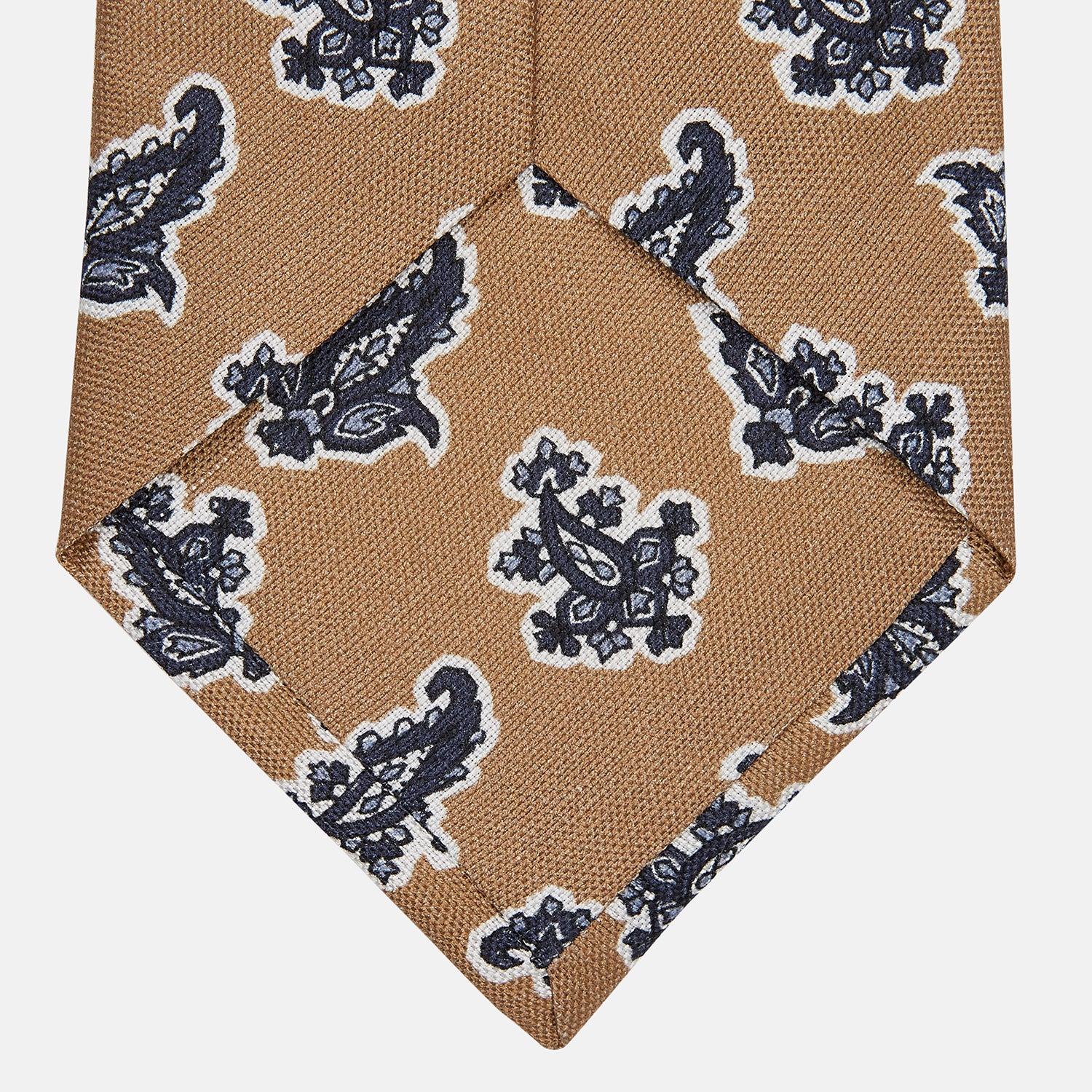 View 3 of product The Turnbull & Asser Toffee Paisley Floral Cotton Silk Blend Tie features a rolled-up design with dark blue and white paisley motifs on a tan background.