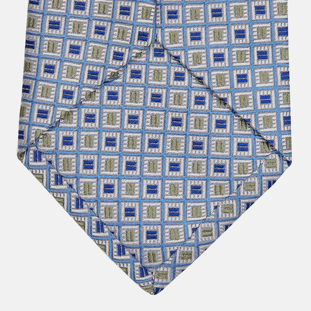 A Turnbull & Asser Blue and Yellow Geometric Silk Jacquard Tie is shown rolled up on a plain light background.