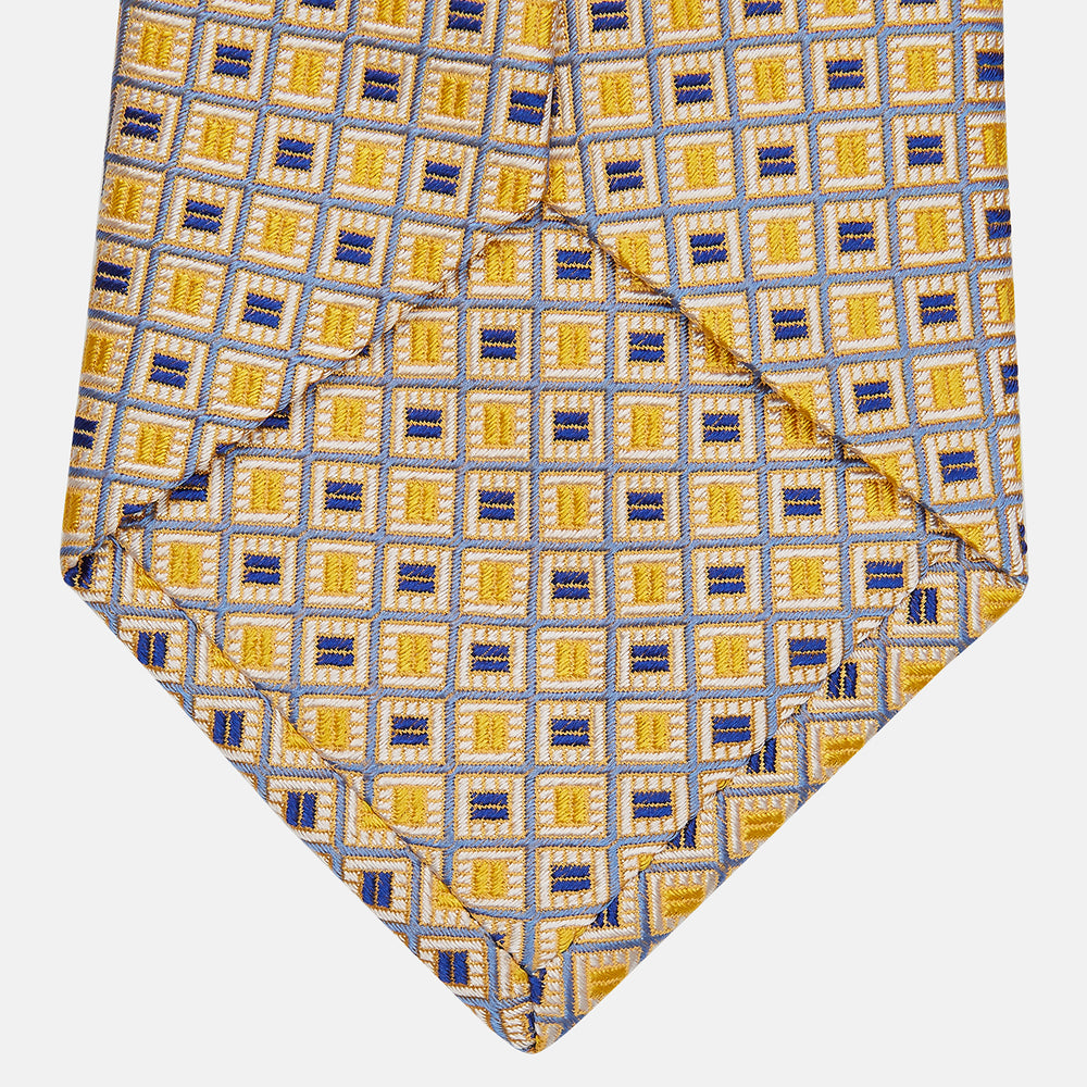 The Turnbull & Asser Yellow and Navy Geometric Silk Jacquard Tie features a striking square pattern on a light background, ideal for formal occasions, shown rolled up against a plain white surface.
