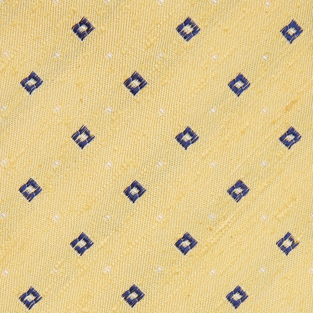 The Turnbull & Asser Yellow Fine Square Slub Silk Tie features a soft yellow jacquard with a subtle texture, decorated with a repeating blue and white diamond pattern, shown rolled up on a plain white background.