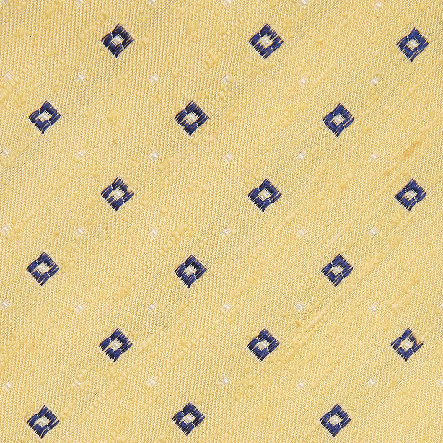 View 2 of product The Turnbull & Asser Yellow Fine Square Slub Silk Tie features a soft yellow jacquard with a subtle texture, decorated with a repeating blue and white diamond pattern, shown rolled up on a plain white background.