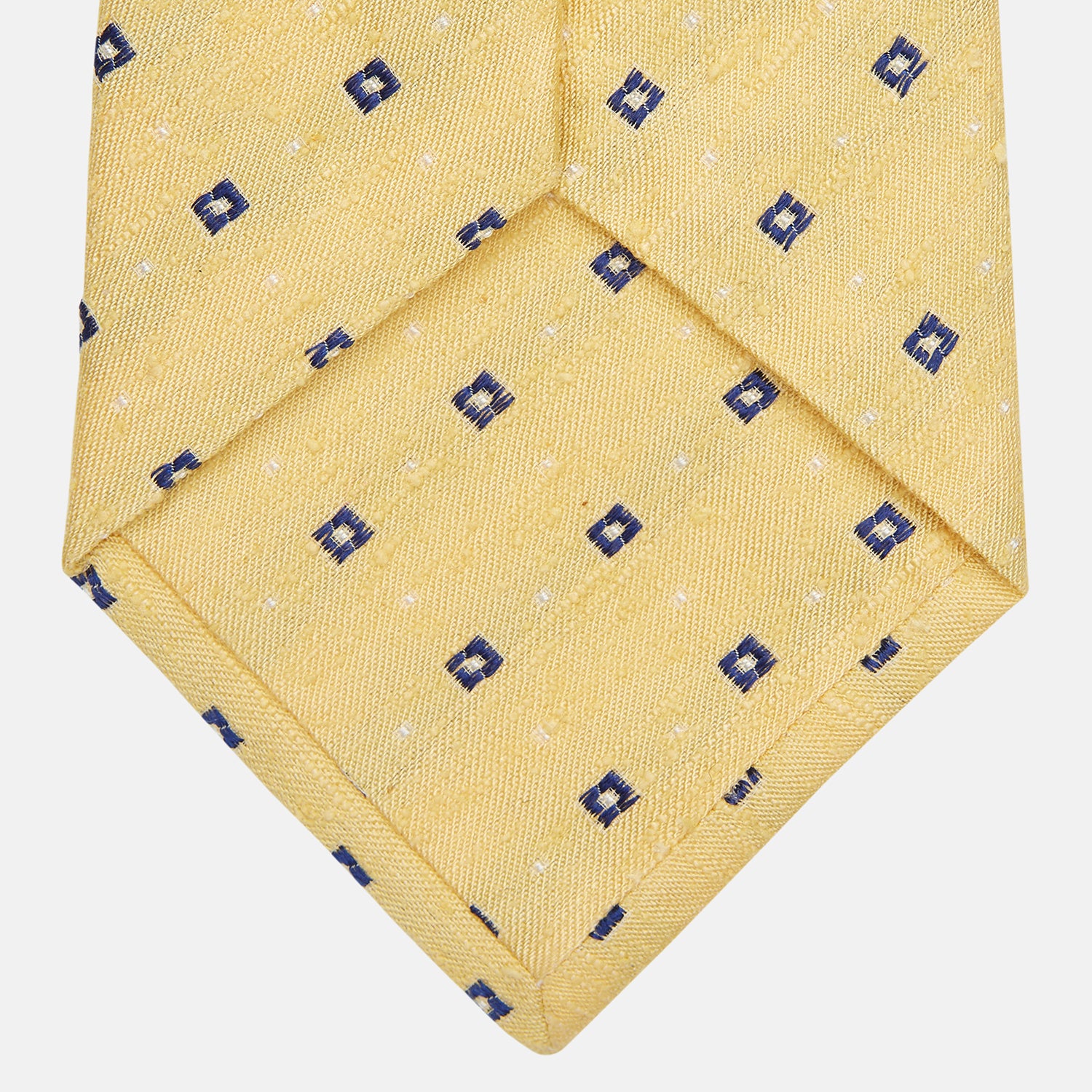 View 3 of product The Turnbull & Asser Yellow Fine Square Slub Silk Tie features a soft yellow jacquard with a subtle texture, decorated with a repeating blue and white diamond pattern, shown rolled up on a plain white background.