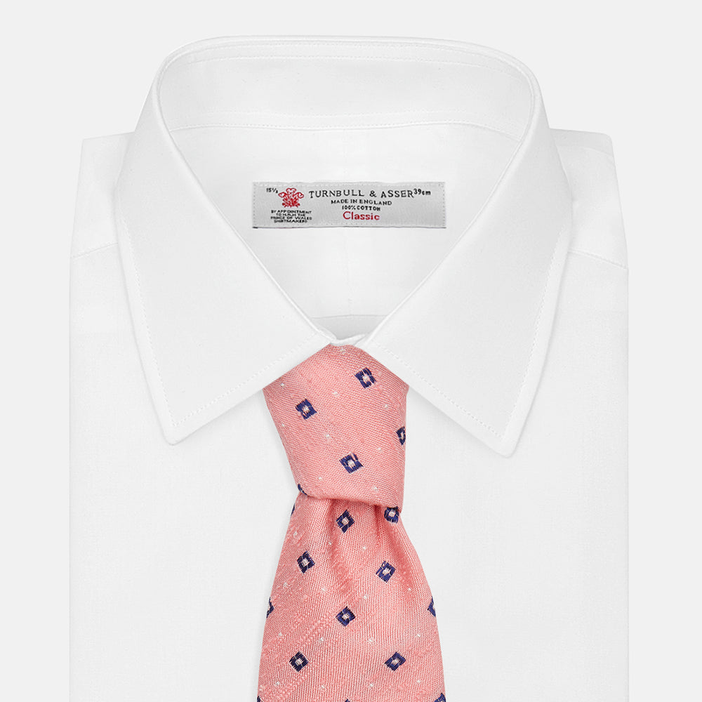 The Turnbull & Asser Pink Fine Square Slub Silk Tie features a pastel pink silk jacquard with blue and white geometric squares, shown rolled up on a plain white background.