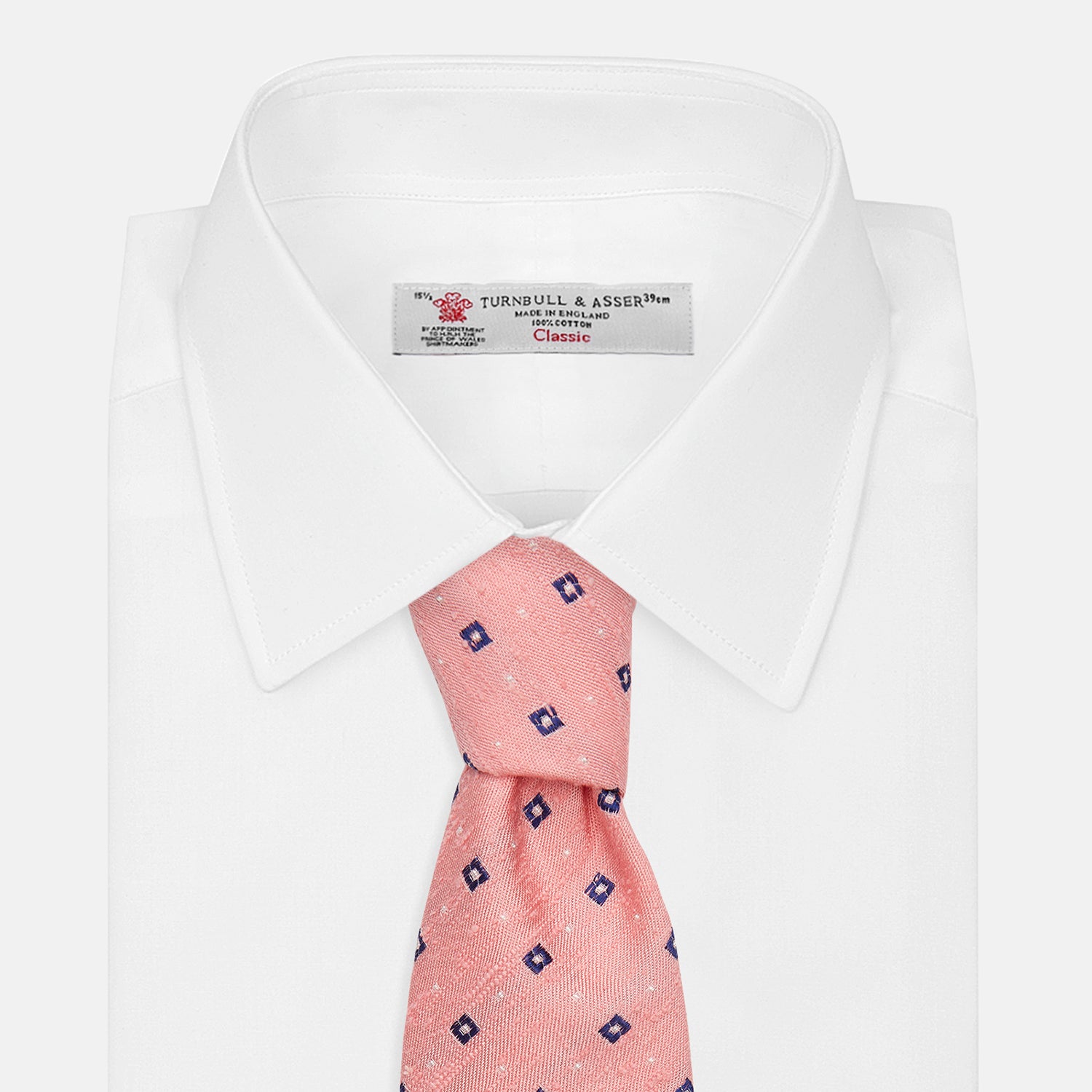 View 4 of product The Turnbull & Asser Pink Fine Square Slub Silk Tie features a pastel pink silk jacquard with blue and white geometric squares, shown rolled up on a plain white background.