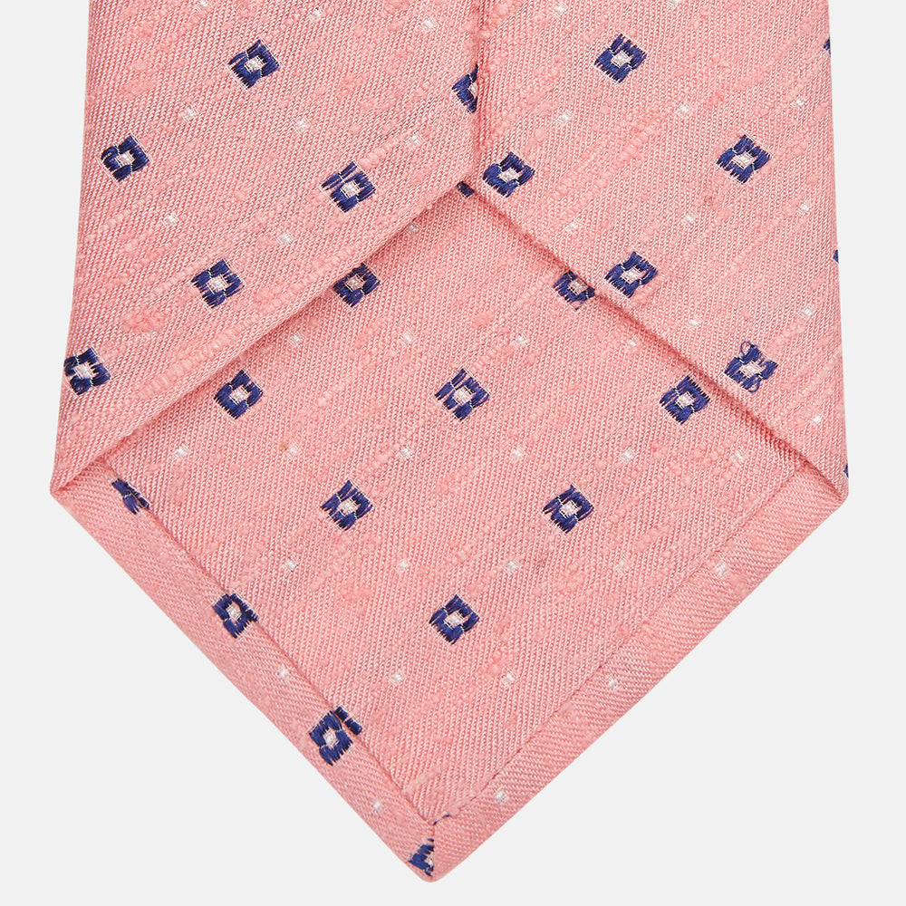 The Turnbull & Asser Pink Fine Square Slub Silk Tie features a pastel pink silk jacquard with blue and white geometric squares, shown rolled up on a plain white background.
