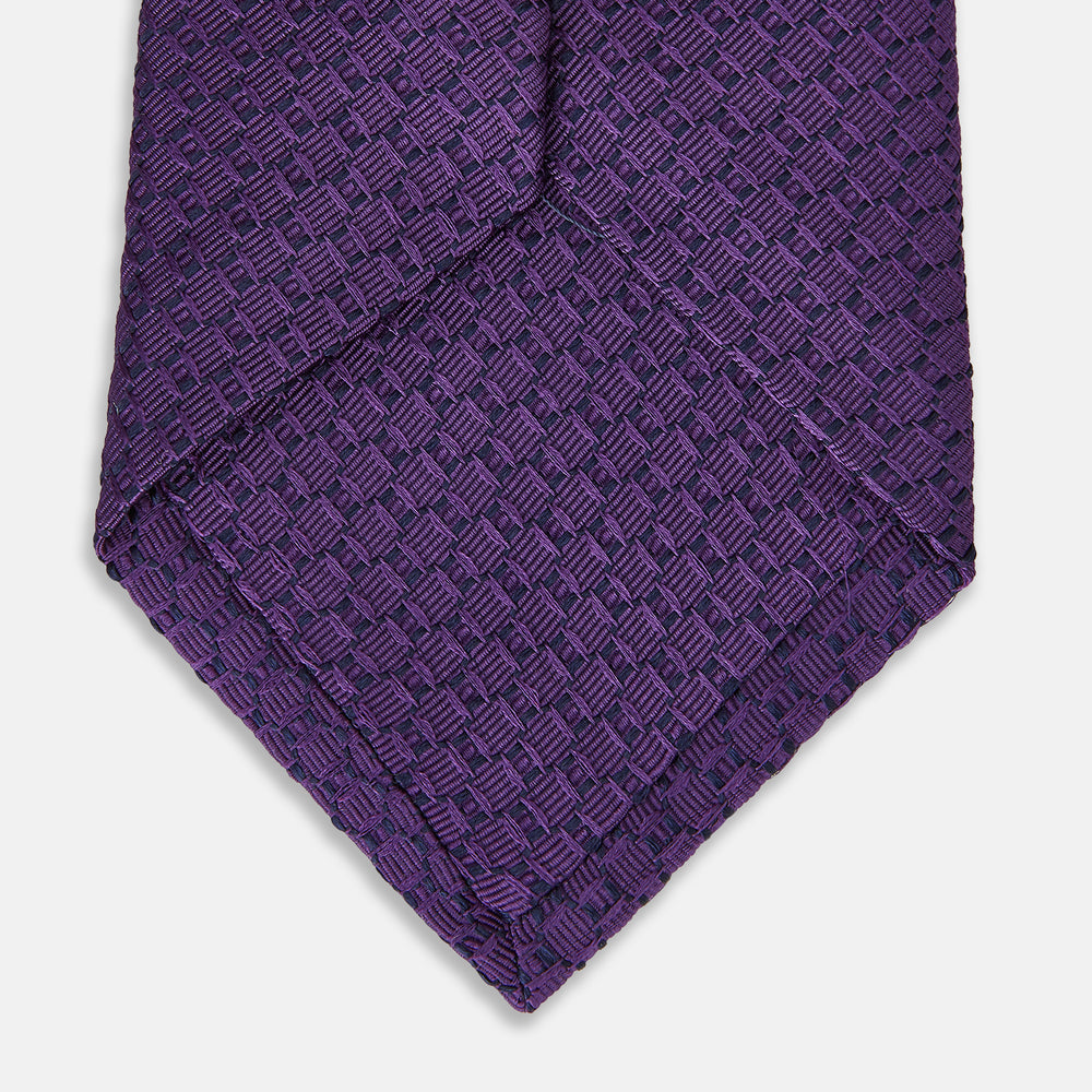 The Turnbull & Asser Purple Abstract Tonal Silk Jacquard Tie, featuring a textured geometric pattern, is shown rolled up against a white background—an ideal choice to elevate any formal outfit.