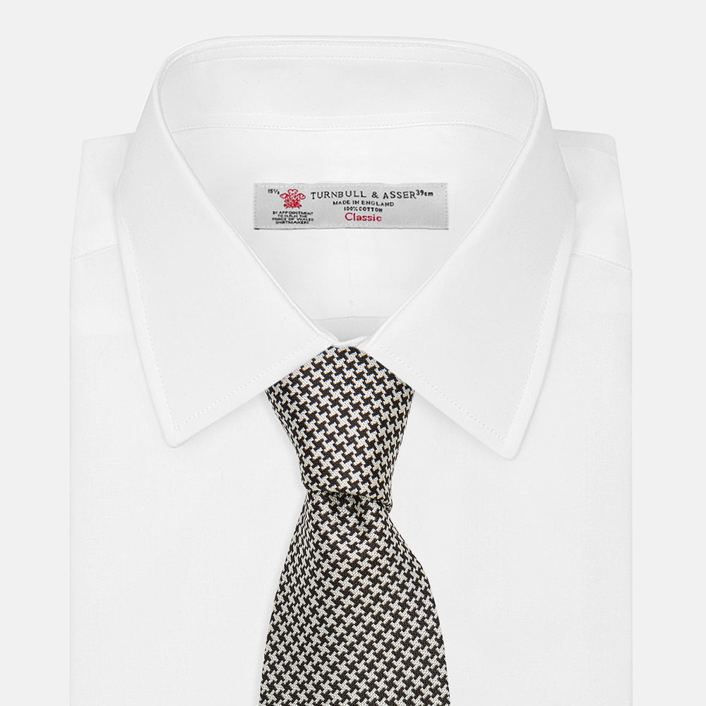 The Turnbull & Asser Fine Puppytooth Monochrome Silk Tie, in classic black and white, features a refined pattern and is shown rolled on a plain white background—ideal for enhancing any formal outfit.