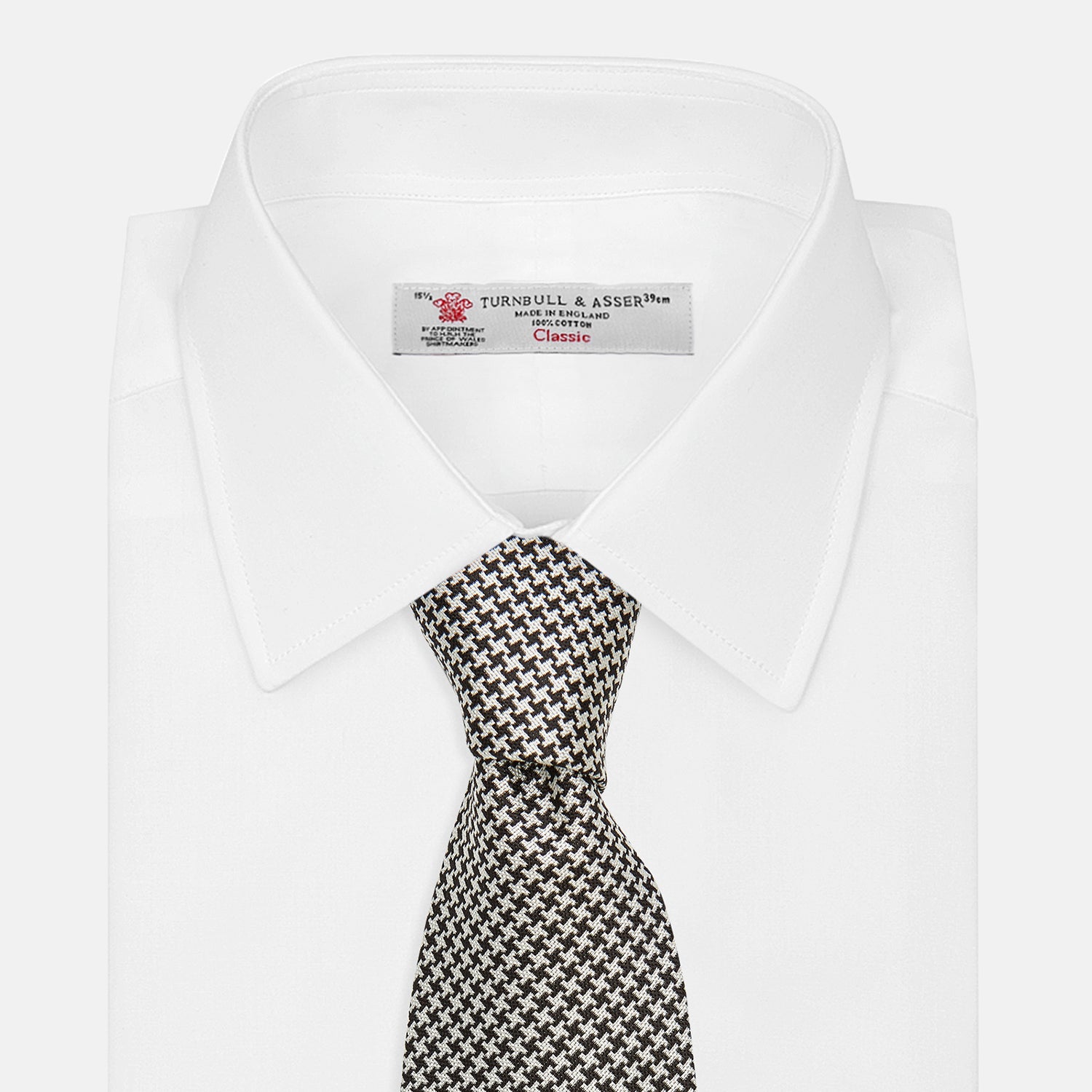 View 4 of product The Turnbull & Asser Fine Puppytooth Monochrome Silk Tie, in classic black and white, features a refined pattern and is shown rolled on a plain white background—ideal for enhancing any formal outfit.