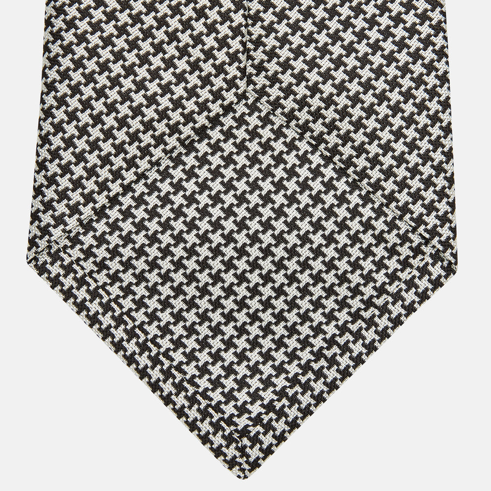 The Turnbull & Asser Fine Puppytooth Monochrome Silk Tie, in classic black and white, features a refined pattern and is shown rolled on a plain white background—ideal for enhancing any formal outfit.