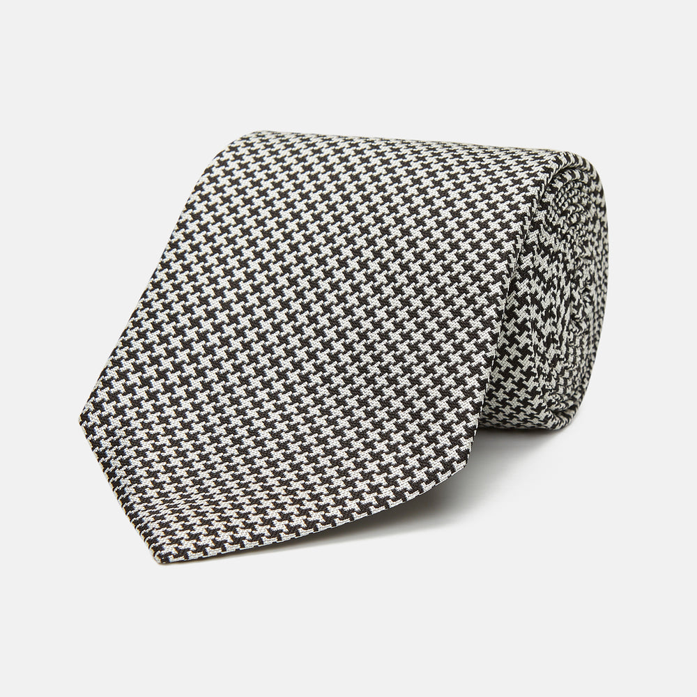 The Turnbull & Asser Fine Puppytooth Monochrome Silk Tie, in classic black and white, features a refined pattern and is shown rolled on a plain white background—ideal for enhancing any formal outfit.