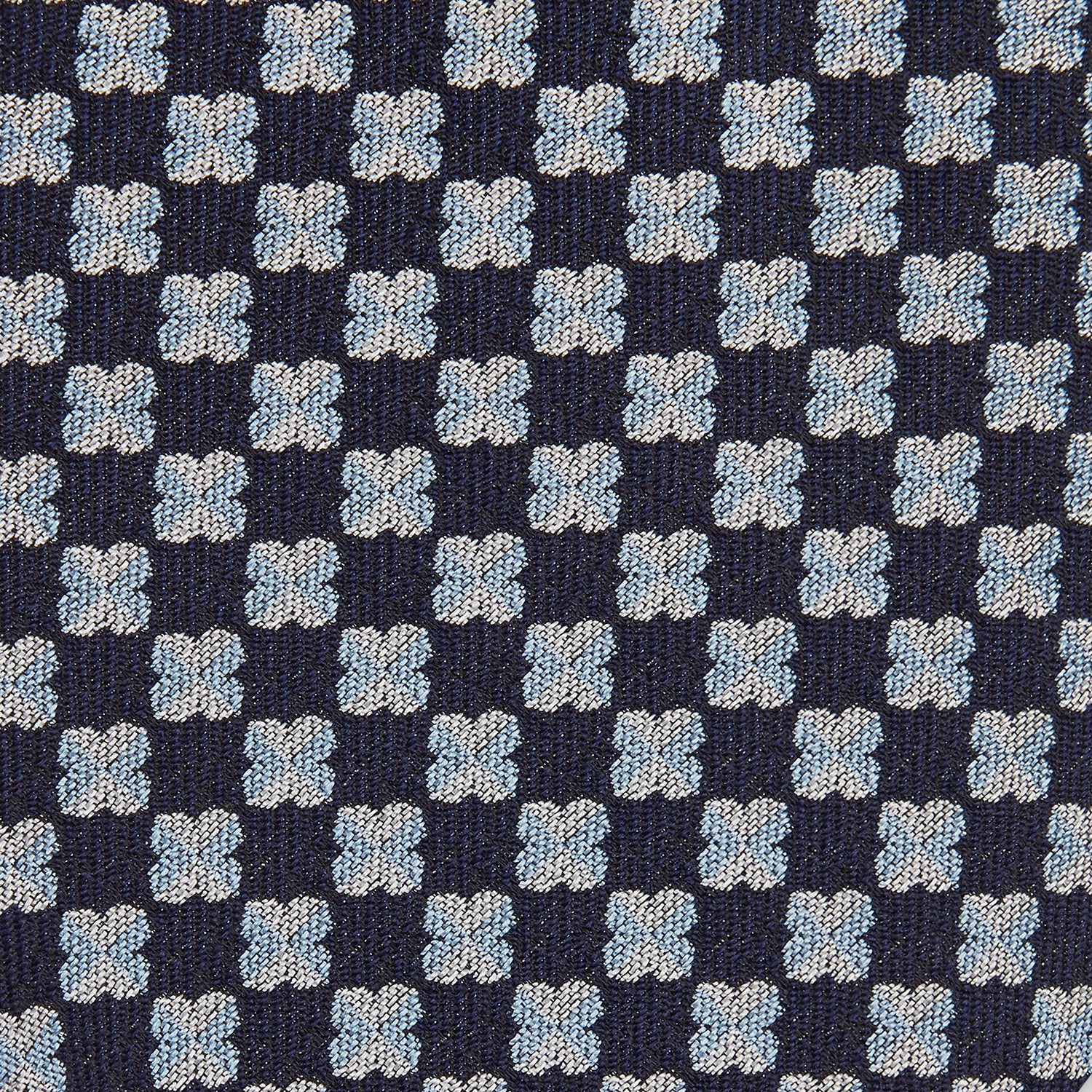 View 2 of product The Turnbull & Asser Indigo Graphic Floral Silk Jacquard Tie features a repeating pattern of light blue and white geometric shapes, shown rolled up on a plain white background.
