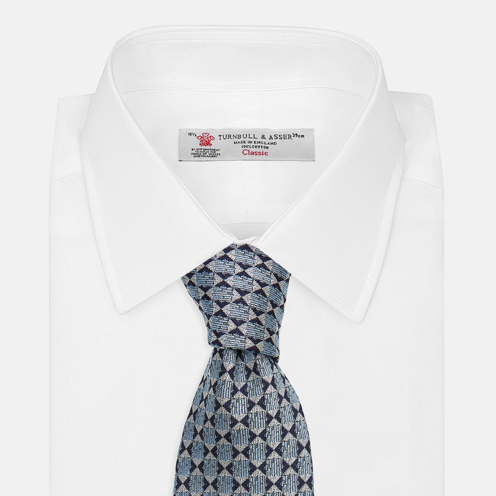 The Chambray Blue Graphic Floral Silk Jacquard Tie by Turnbull & Asser features a modern floral pattern in silk, shown rolled up against a plain white background.