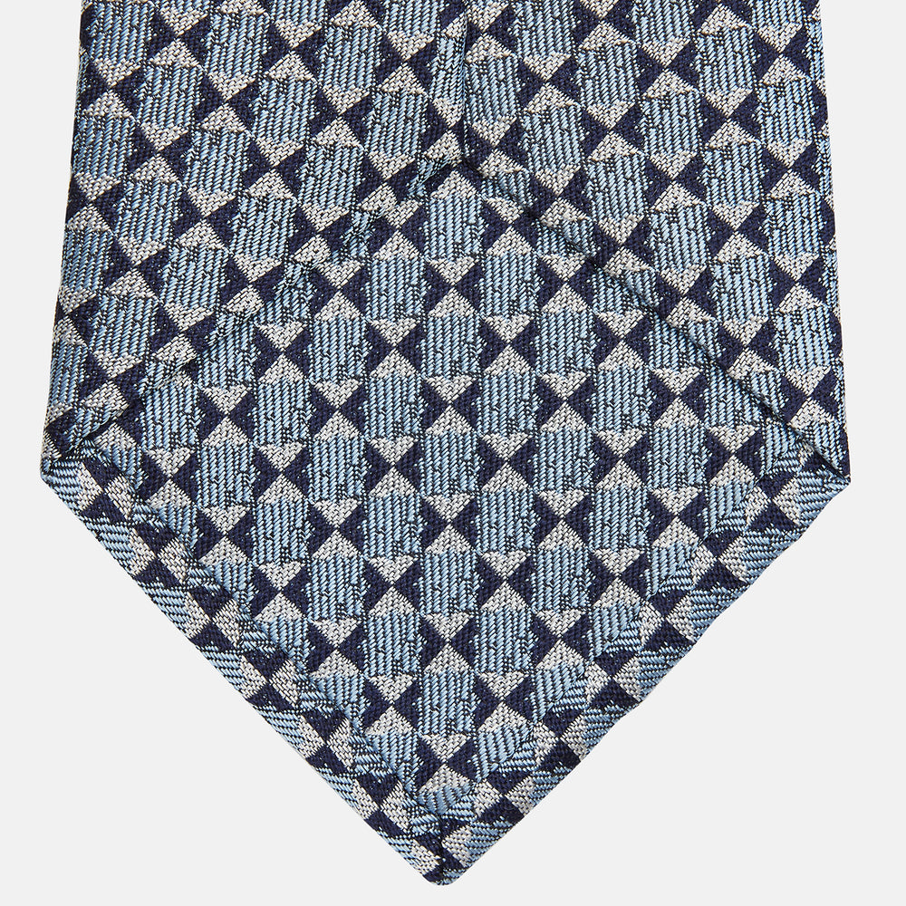 The Chambray Blue Graphic Floral Silk Jacquard Tie by Turnbull & Asser features a modern floral pattern in silk, shown rolled up against a plain white background.
