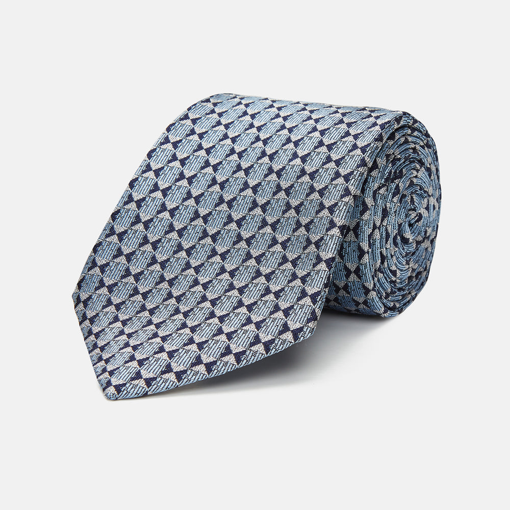 The Chambray Blue Graphic Floral Silk Jacquard Tie by Turnbull & Asser features a modern floral pattern in silk, shown rolled up against a plain white background.
