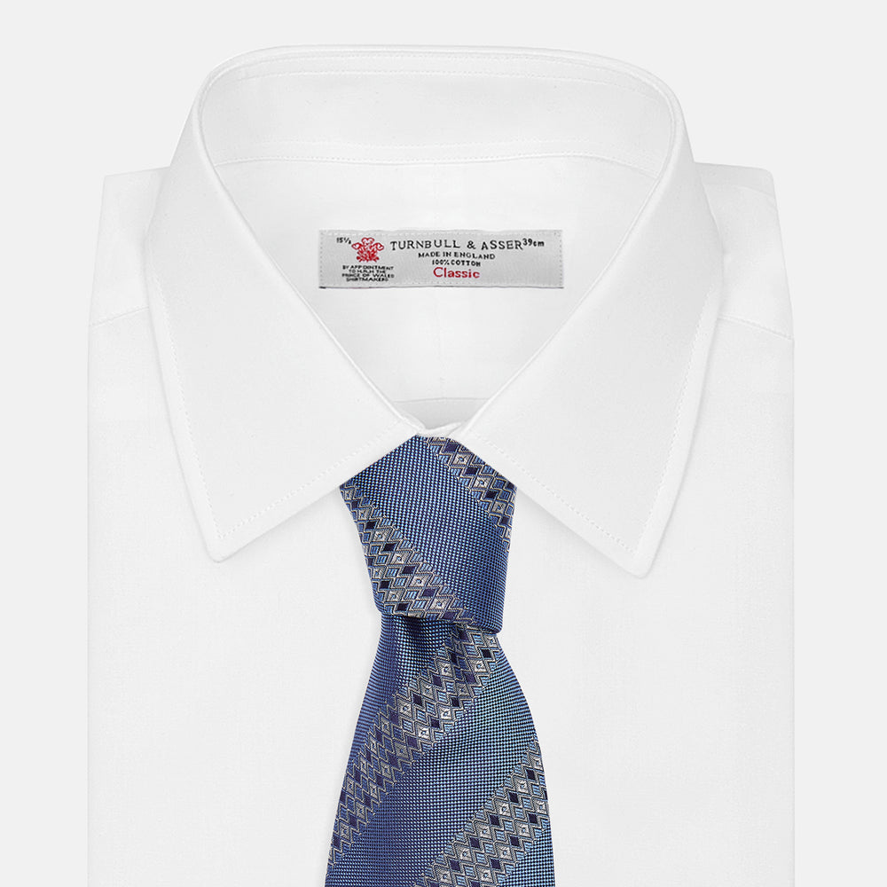 The Turnbull & Asser Dark Blue Baroque Stripe Silk Jacquard Tie, featuring elegant baroque stripes, is displayed rolled up on a white background.