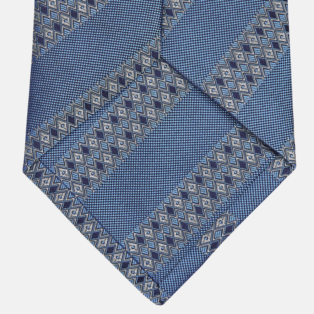 The Turnbull & Asser Dark Blue Baroque Stripe Silk Jacquard Tie, featuring elegant baroque stripes, is displayed rolled up on a white background.