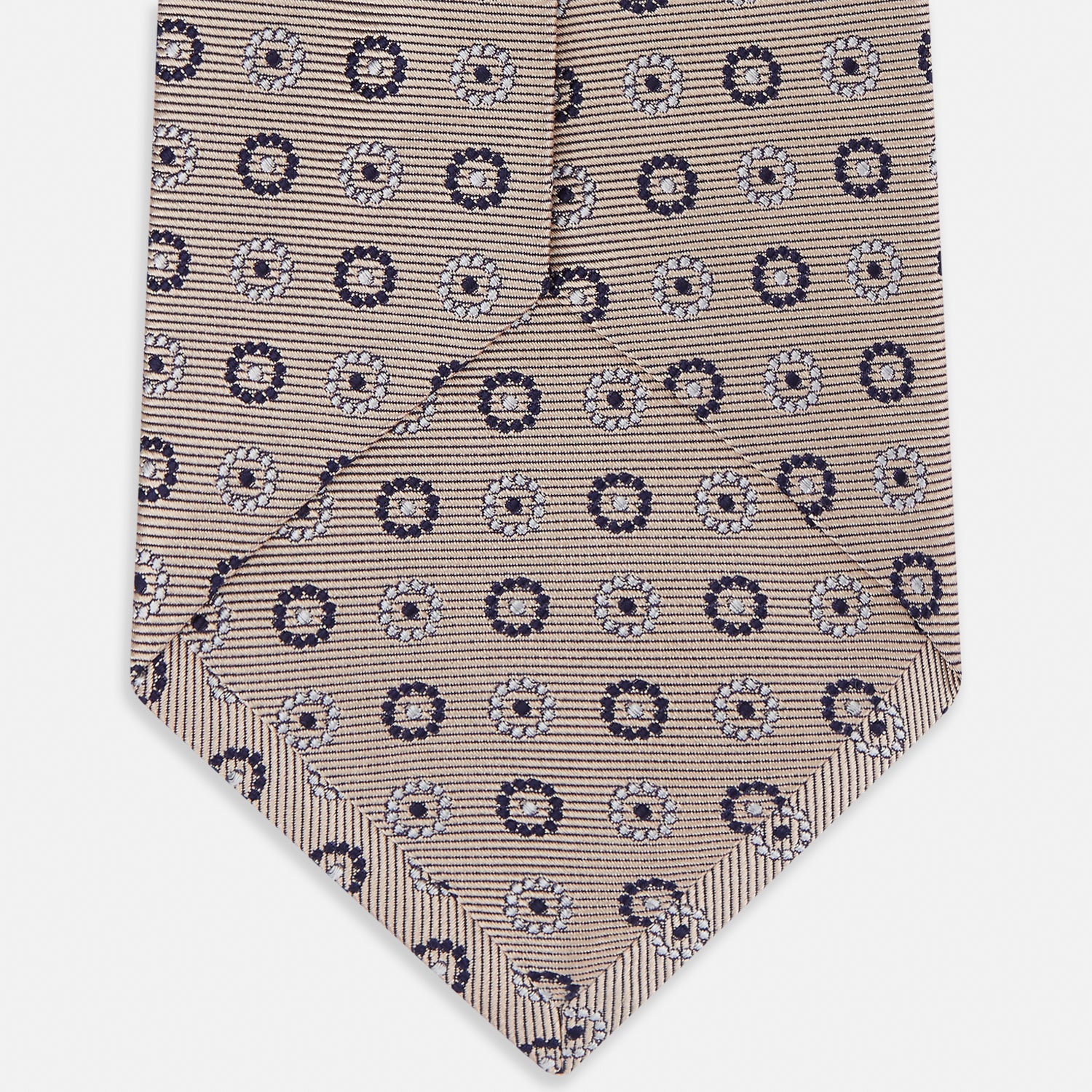 View 4 of product The Turnbull & Asser Beige Spheric Emblem Tie, a formalwear essential, features a neat roll and a repeating pattern of navy and white circular floral motifs on pastel beige.