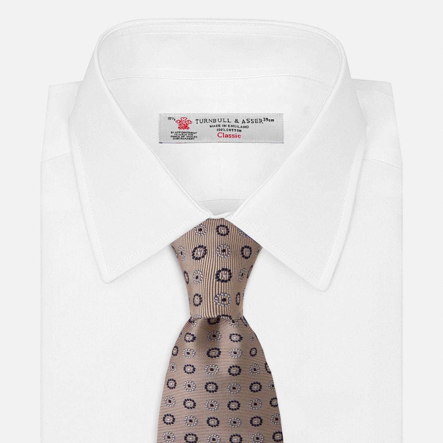 View 2 of product The Turnbull & Asser Beige Spheric Emblem Tie, a formalwear essential, features a neat roll and a repeating pattern of navy and white circular floral motifs on pastel beige.