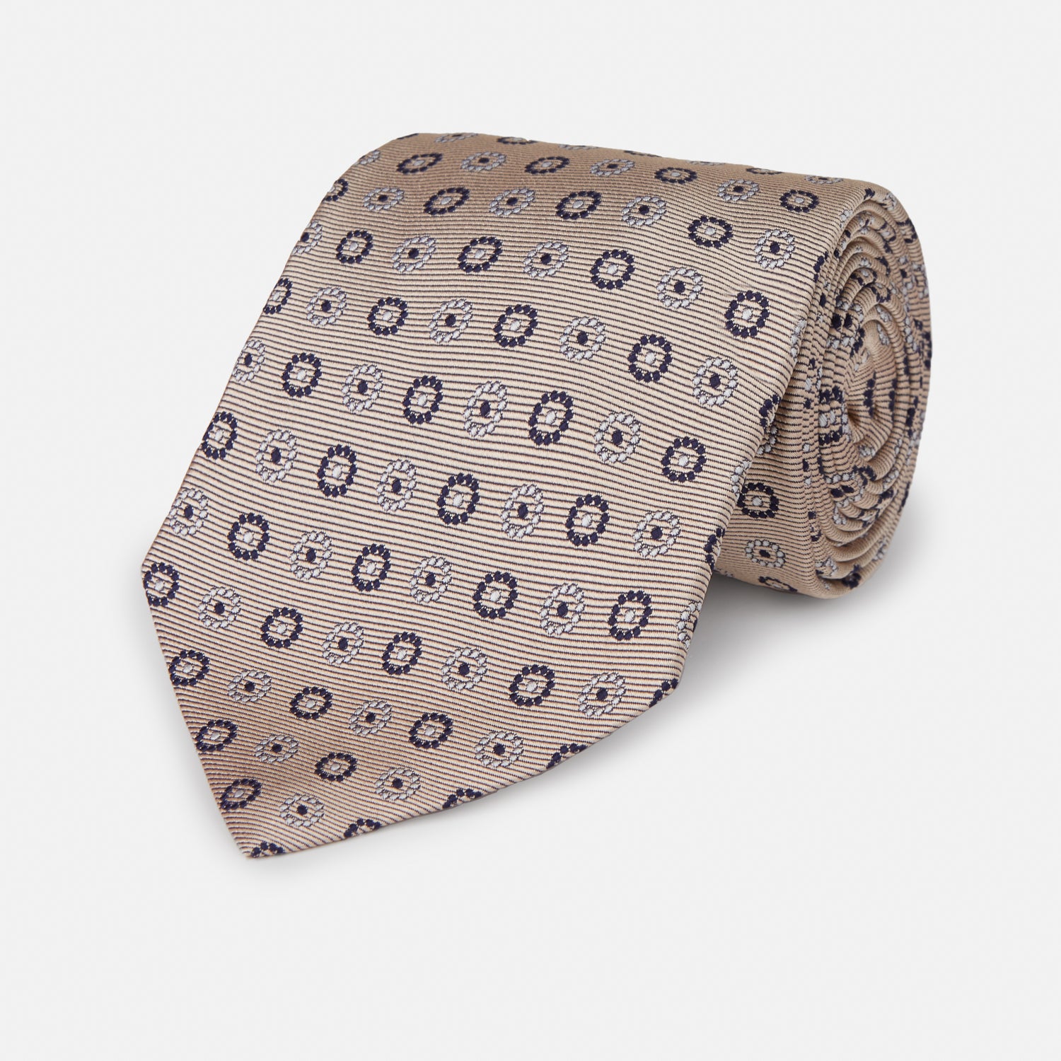 View 1 of product The Turnbull & Asser Beige Spheric Emblem Tie, a formalwear essential, features a neat roll and a repeating pattern of navy and white circular floral motifs on pastel beige.