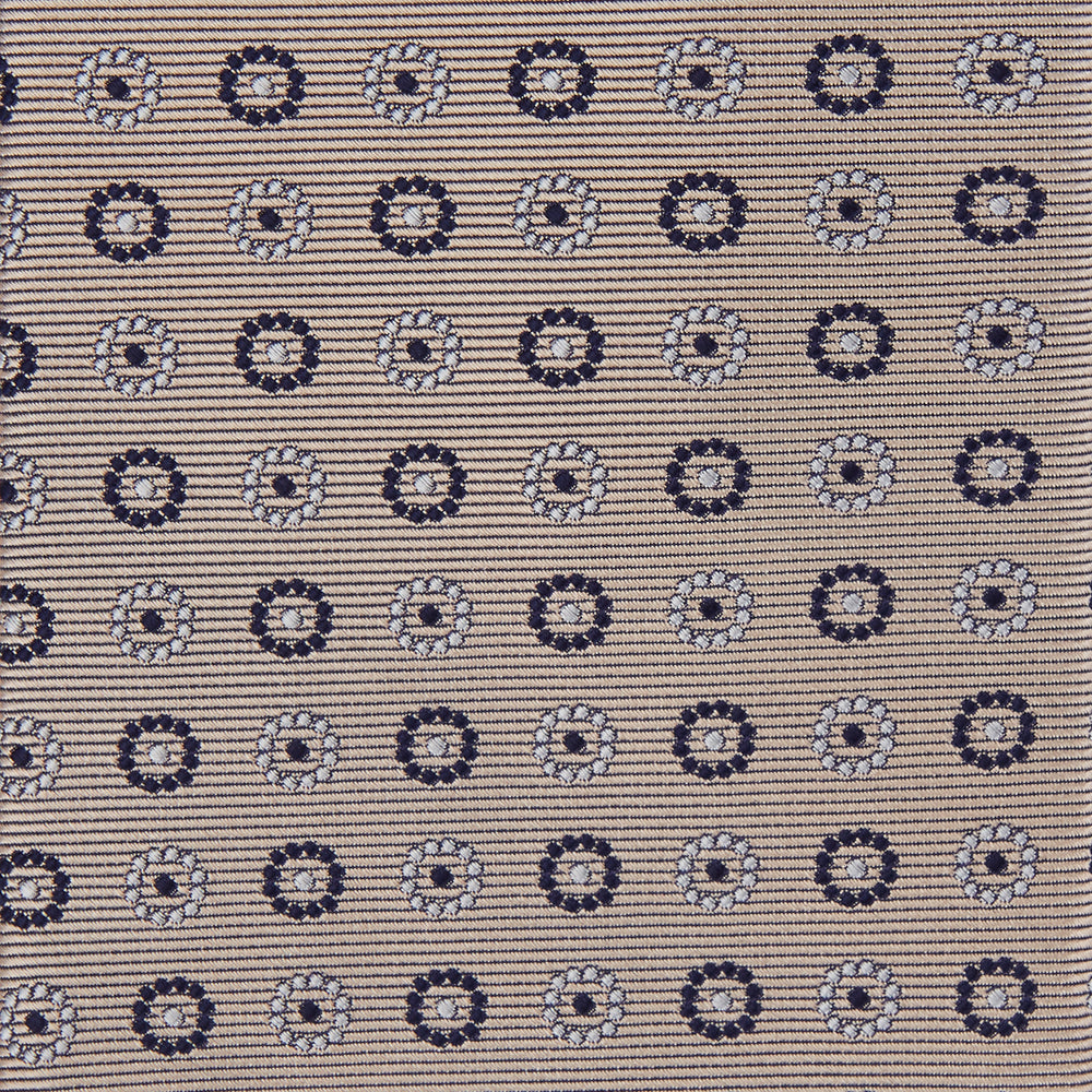 The Turnbull & Asser Beige Spheric Emblem Tie, a formalwear essential, features a neat roll and a repeating pattern of navy and white circular floral motifs on pastel beige.