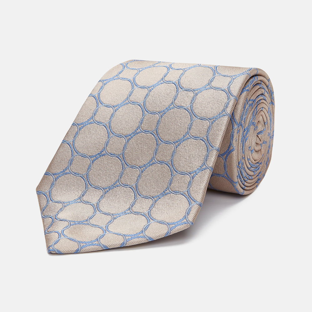 The Turnbull & Asser Toffee and Powder Blue Circle Jacquard Silk Tie, featuring an interlocking circular pattern, is rolled up and displayed on a plain white background.