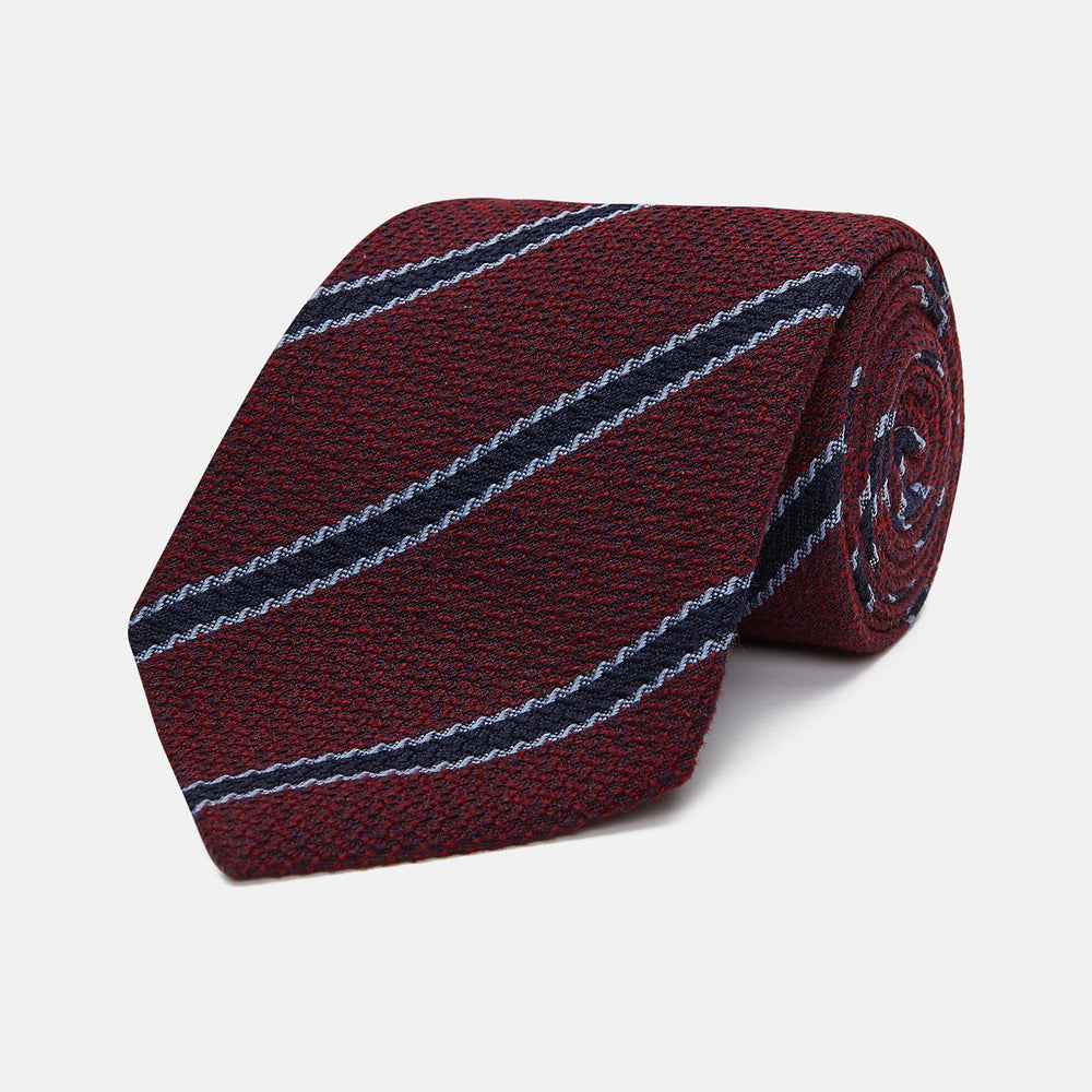 Turnbull & Asser’s Burgundy Stripe Wool and Silk Tie features diagonal navy and light blue stripes on a maroon background, shown rolled up against a plain light backdrop.