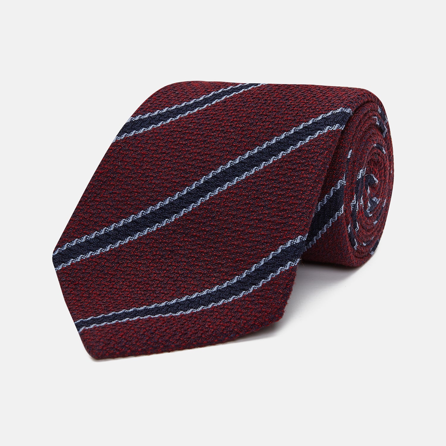 View 1 of product Turnbull & Asser’s Burgundy Stripe Wool and Silk Tie features diagonal navy and light blue stripes on a maroon background, shown rolled up against a plain light backdrop.