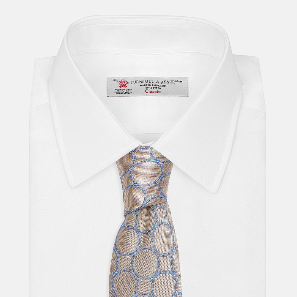 The Turnbull & Asser Toffee and Powder Blue Circle Jacquard Silk Tie, featuring an interlocking circular pattern, is rolled up and displayed on a plain white background.