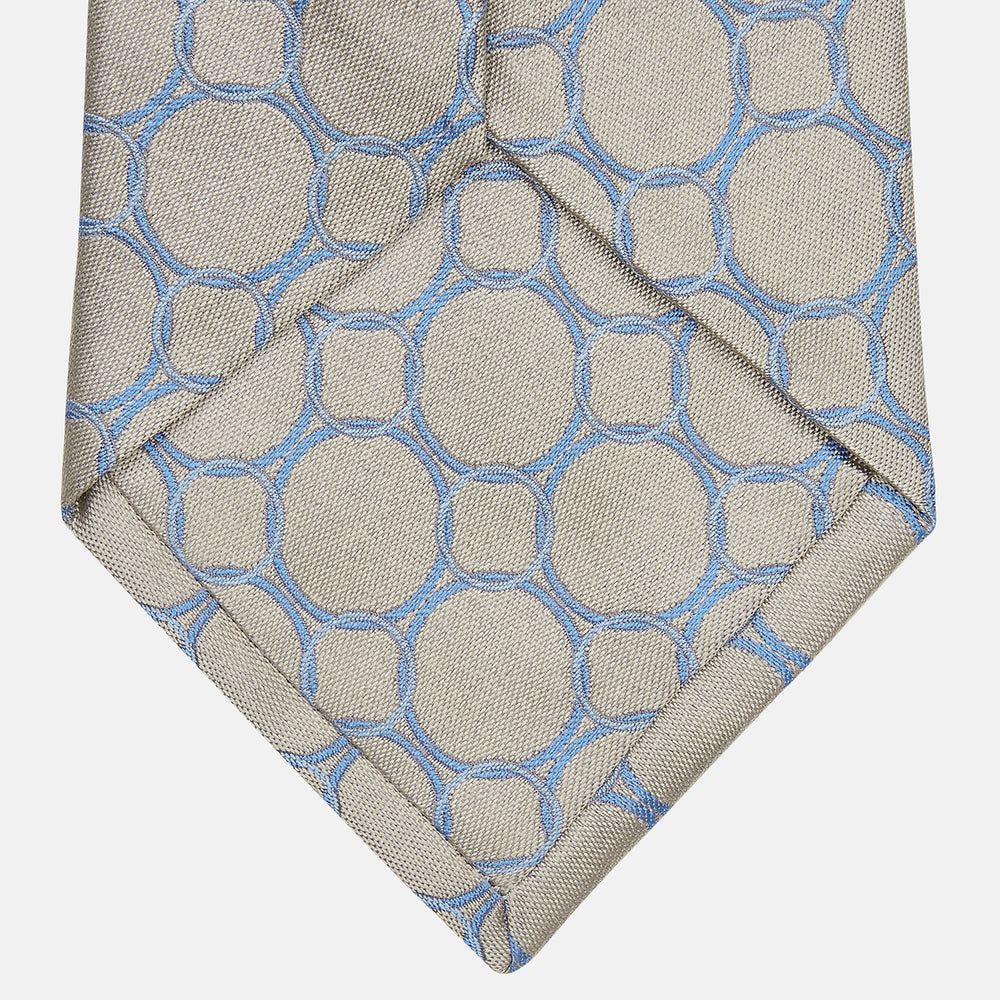 The Turnbull & Asser Toffee and Powder Blue Circle Jacquard Silk Tie, featuring an interlocking circular pattern, is rolled up and displayed on a plain white background.