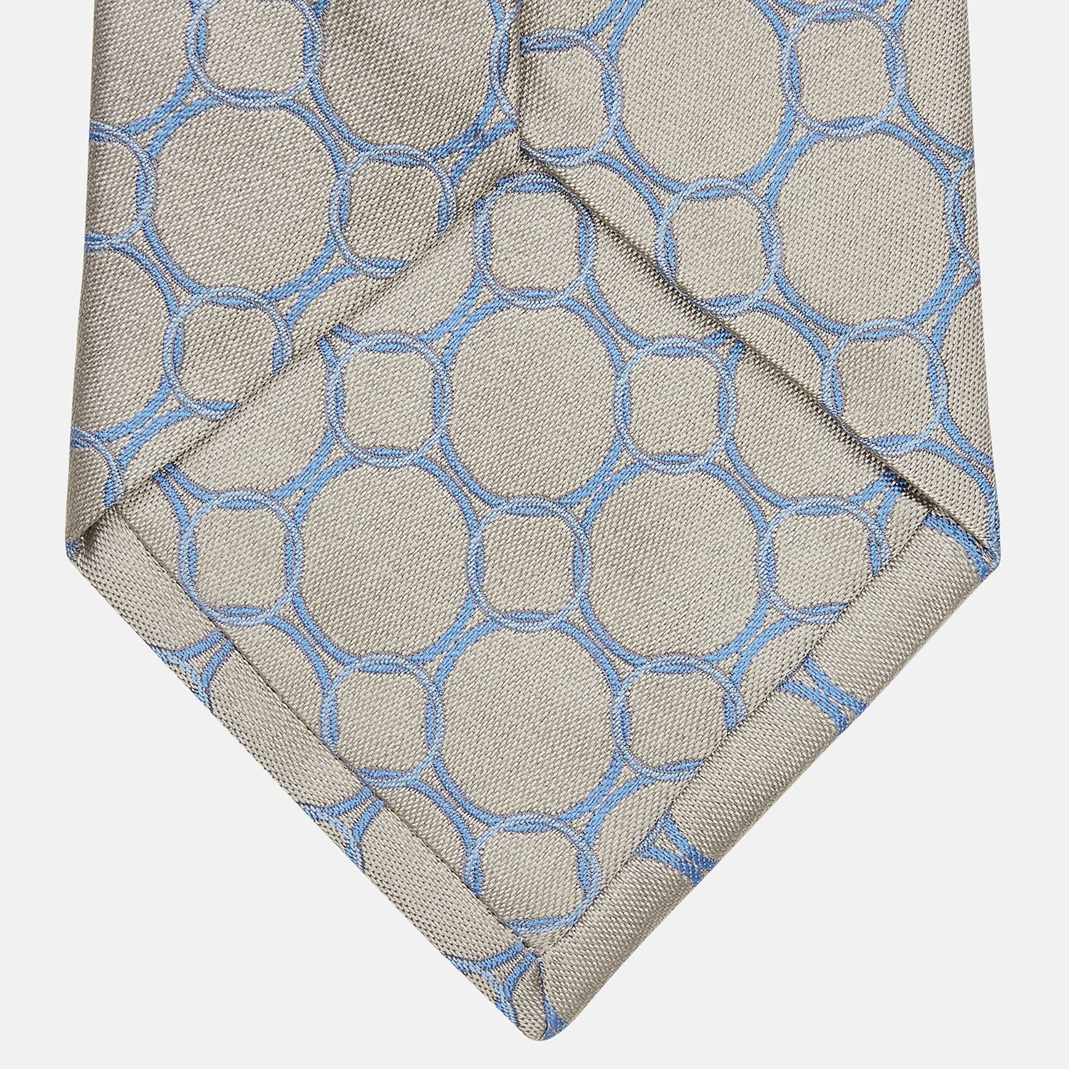 View 3 of product The Turnbull & Asser Toffee and Powder Blue Circle Jacquard Silk Tie, featuring an interlocking circular pattern, is rolled up and displayed on a plain white background.