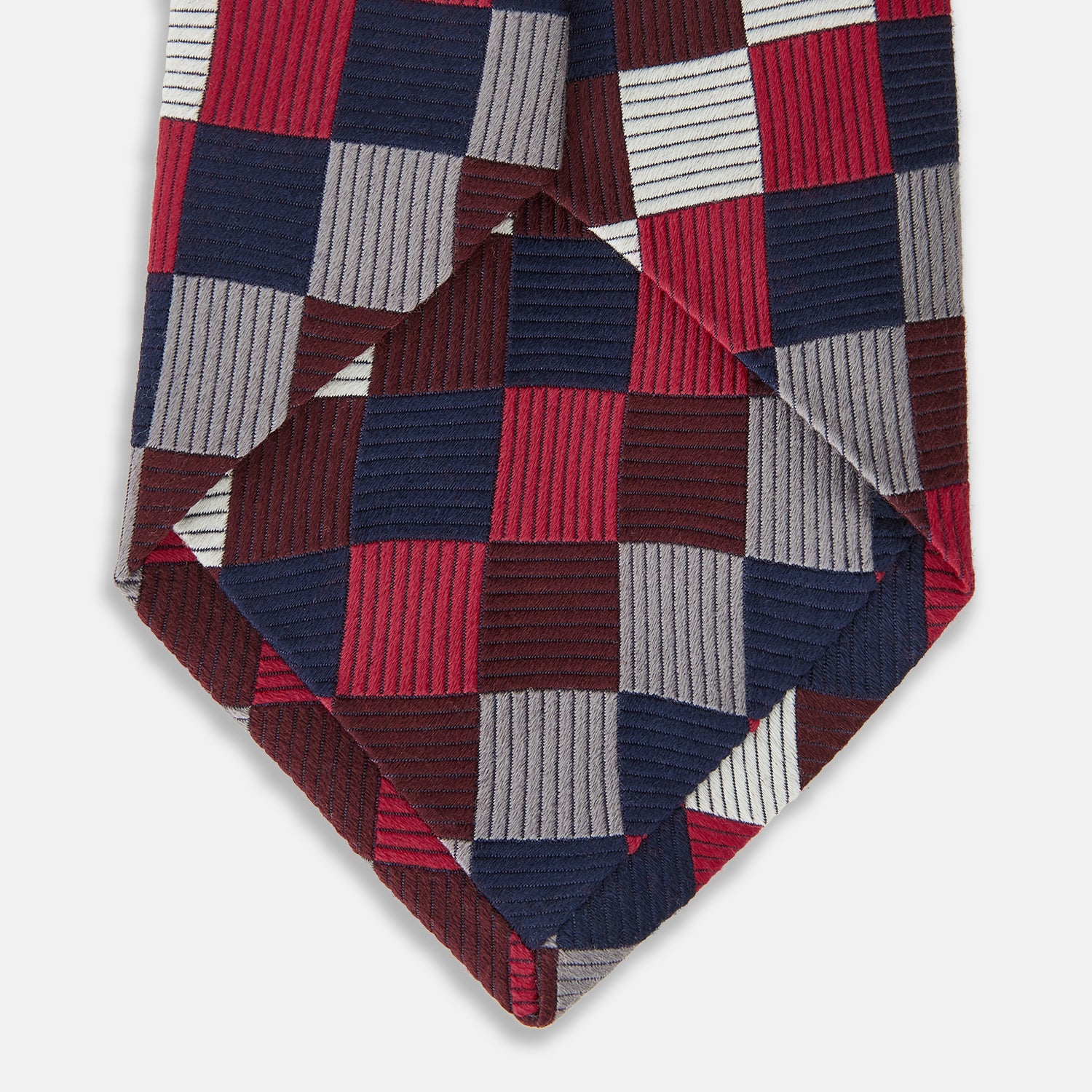 View 4 of product The Burgundy Checkerboard Silk Jacquard Tie by Turnbull & Asser features a bold autumnal pattern in red, navy blue, brown, gray, burgundy, and white squares, shown rolled on a plain white background.