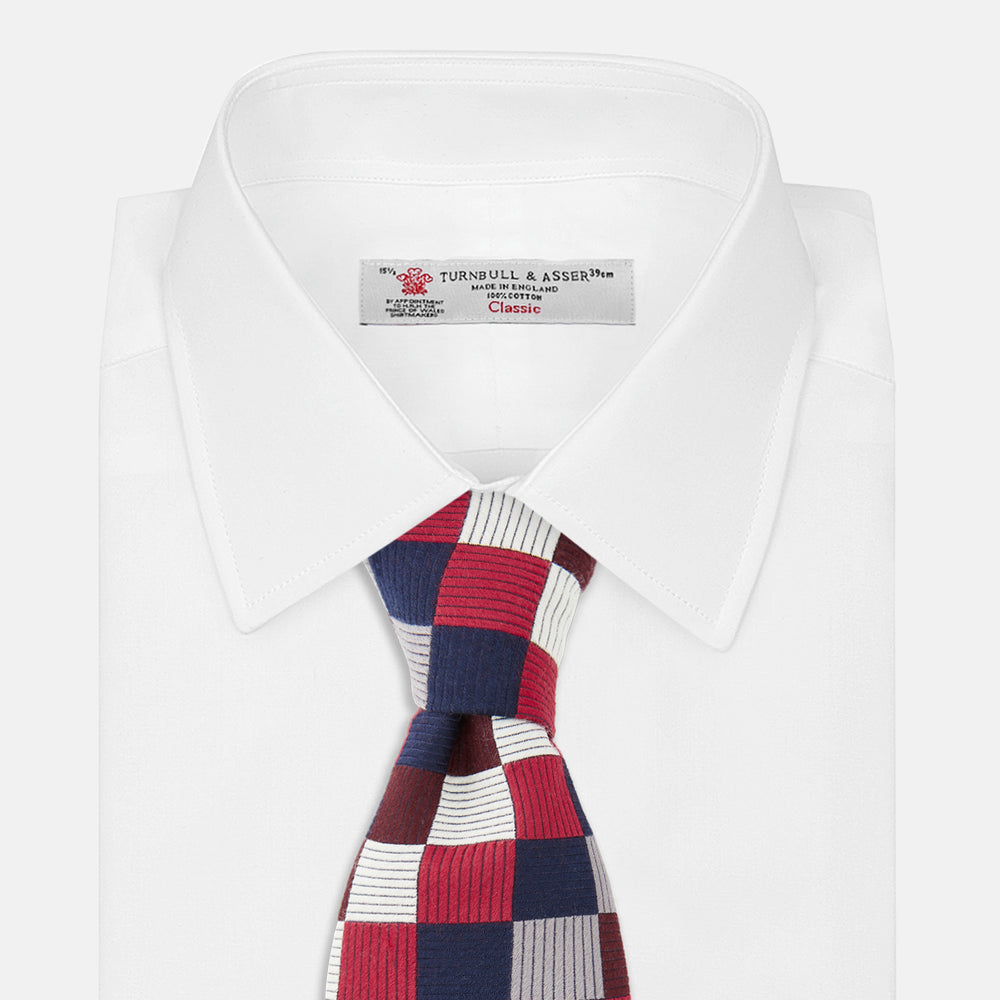 The Burgundy Checkerboard Silk Jacquard Tie by Turnbull & Asser features a bold autumnal pattern in red, navy blue, brown, gray, burgundy, and white squares, shown rolled on a plain white background.