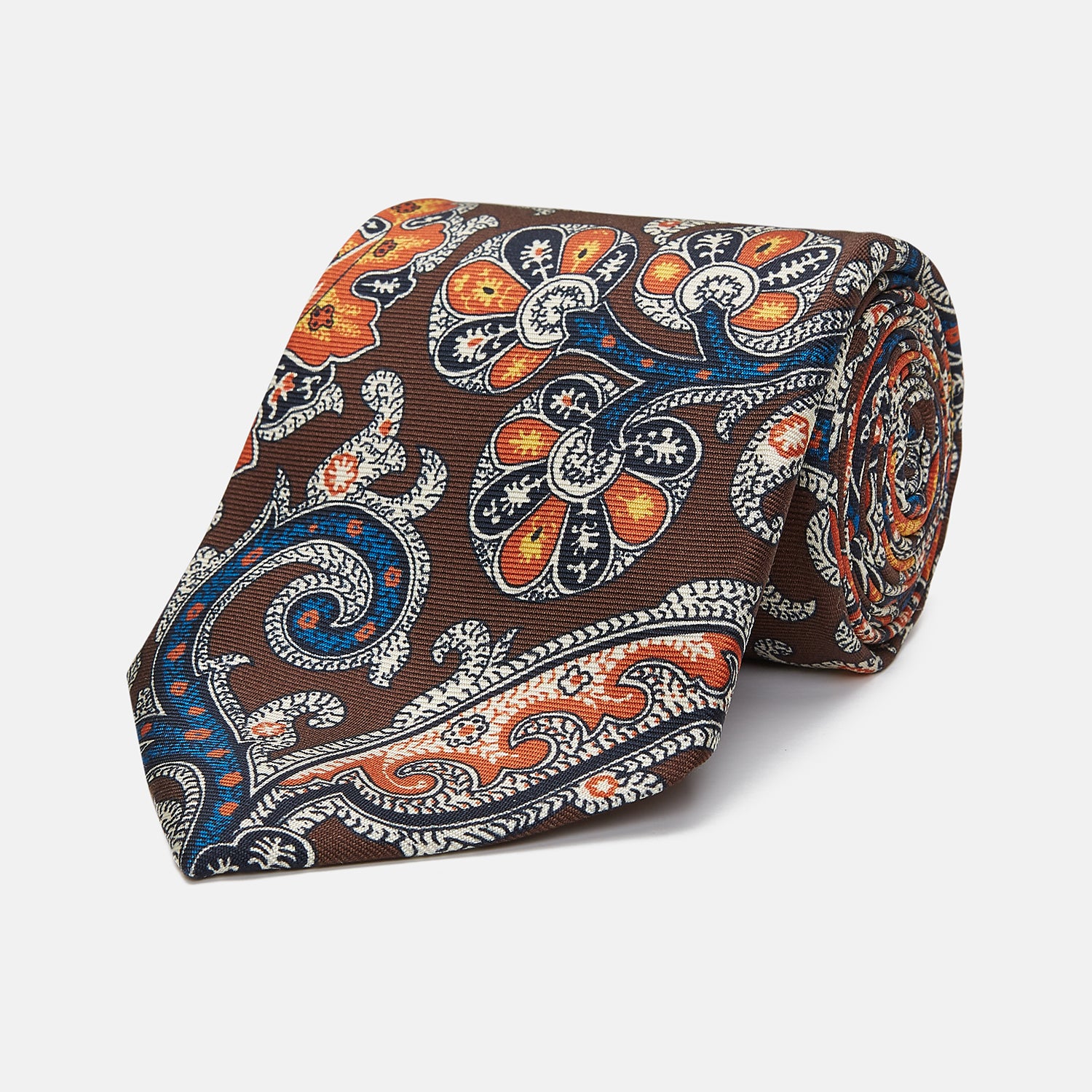 View 1 of product The Turnbull & Asser Chocolate and Orange Twisted Paisley Silk Tie for men showcases a vibrant orange, blue, and white paisley pattern inspired by classic Macclesfield designs, rolled on a plain white background.