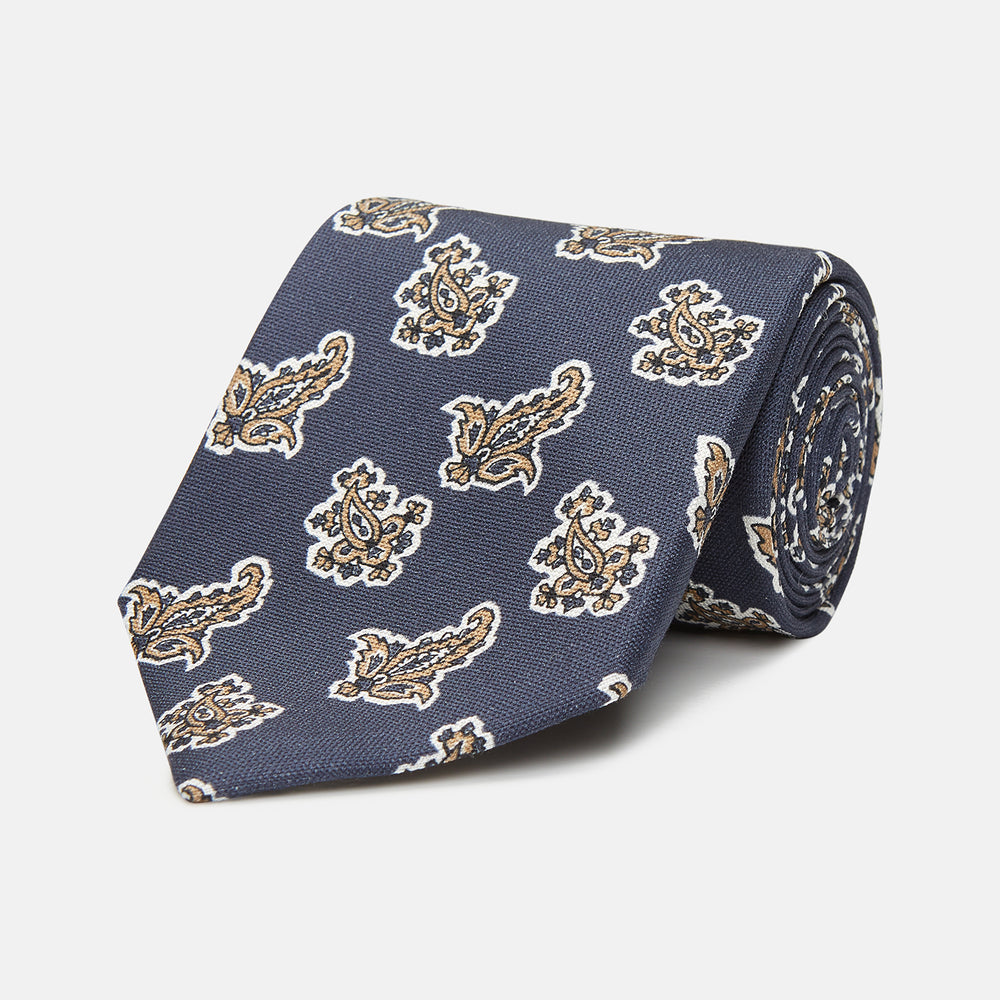 The Turnbull & Asser Navy Paisley Floral Cotton Silk Blend Tie features beige and light blue paisley motifs on navy, with one end rolled.
