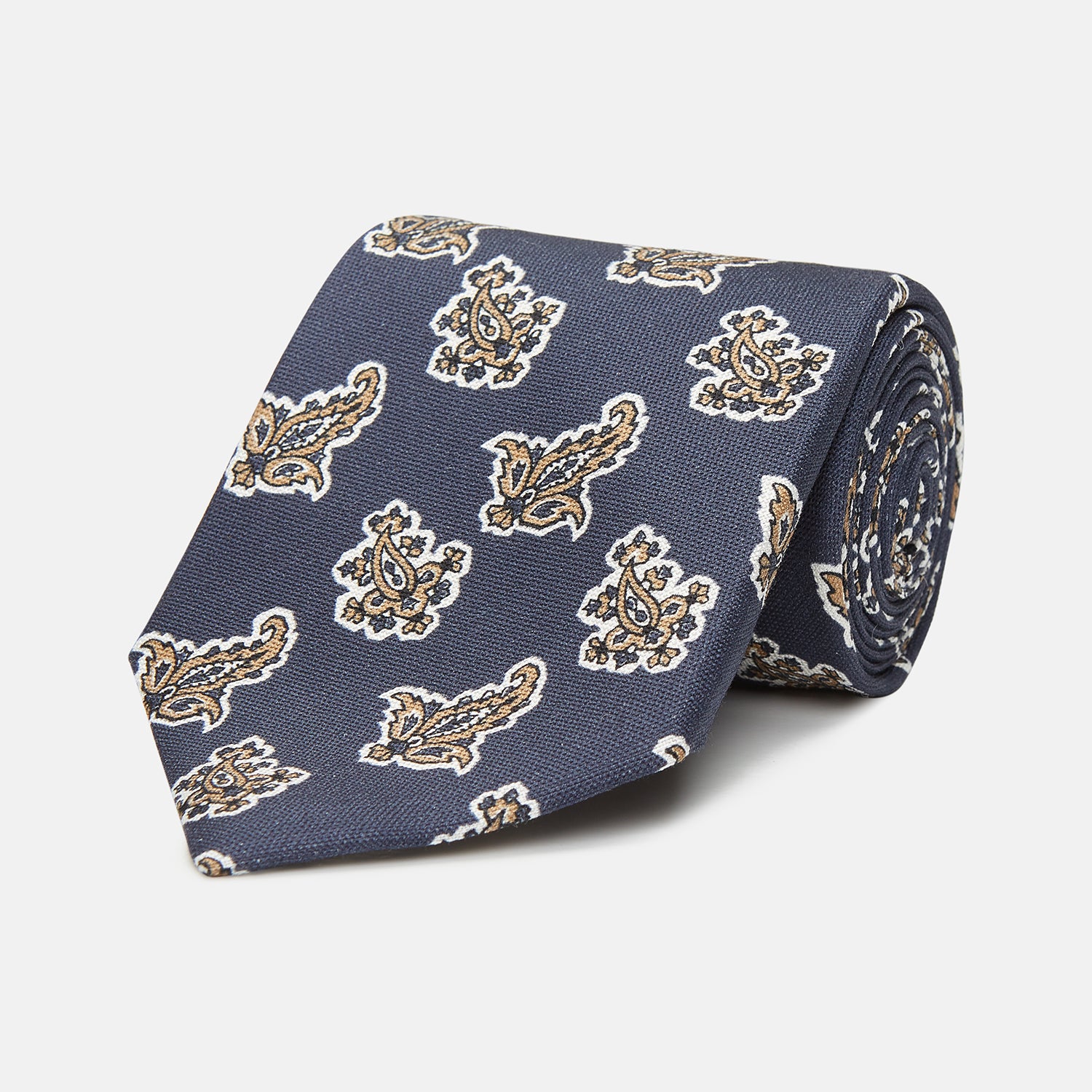 View 1 of product The Turnbull & Asser Navy Paisley Floral Cotton Silk Blend Tie features beige and light blue paisley motifs on navy, with one end rolled.