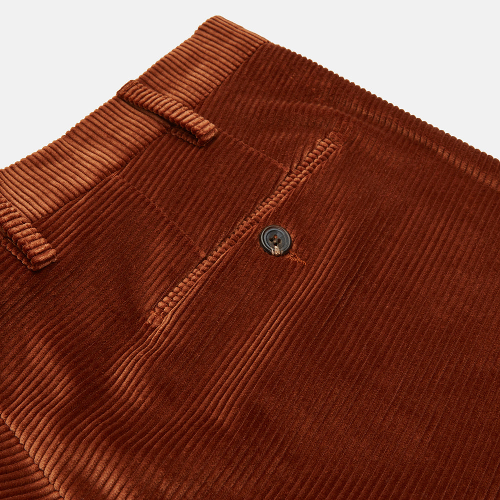 Turnbull & Asser’s Rust Horizontal Cord Trousers feature a straight-leg cut, front pockets, and button closure. Made from heavy-weight corduroy, these trousers are shown laid flat on a white background.