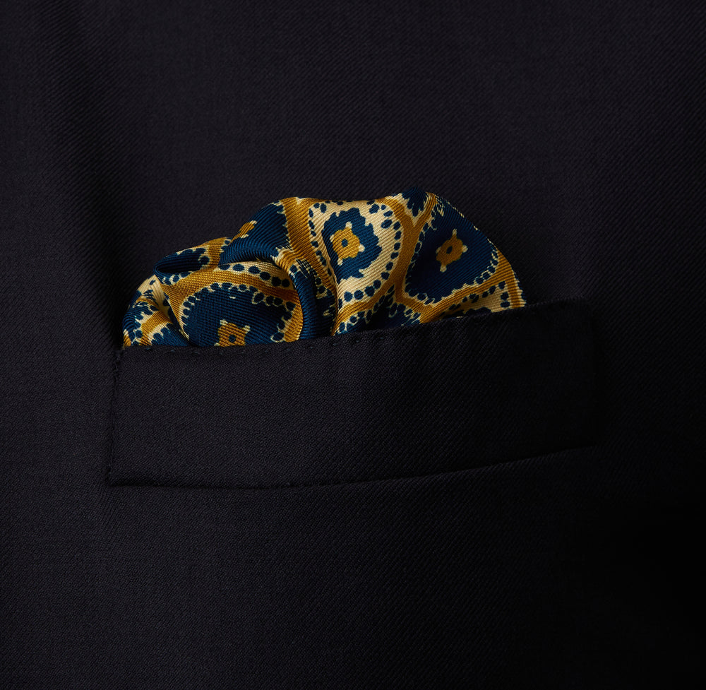 The Tan Medallion Print Silk Pocket Square by Turnbull & Asser features an elegant medallion geometric pattern in blue, white, and gold with central diamond shapes and a gold dotted border on luxurious silk.