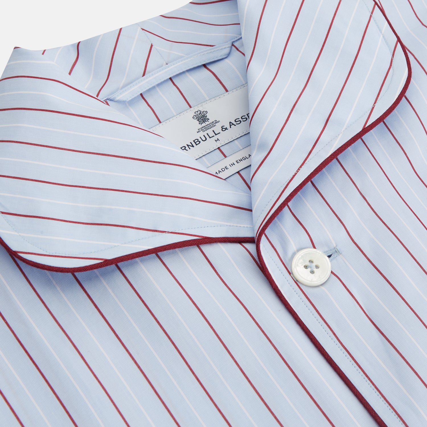 View 2 of product The Turnbull & Asser Burgundy Stripe Classic Pyjama Set features long sleeves, a button-up top with red piping, matching drawstring pants, and a traditional fit. Laid flat, it's luxury loungewear in signature burgundy stripes.
