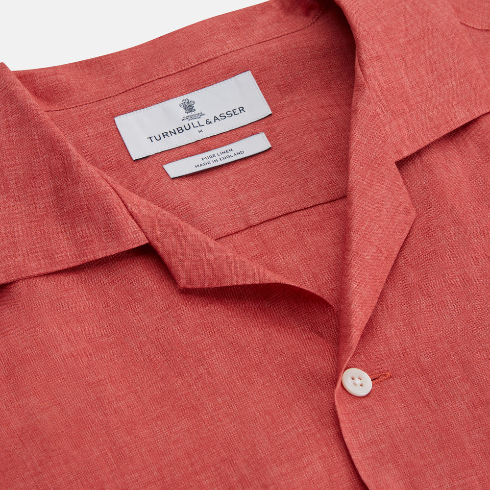 The Turnbull & Asser Crimson Delave Linen Holiday Fit Shirt features a solid brick-red hue, short sleeves, single chest pocket, and revere collar—perfect resort wear—shown laid flat on white.