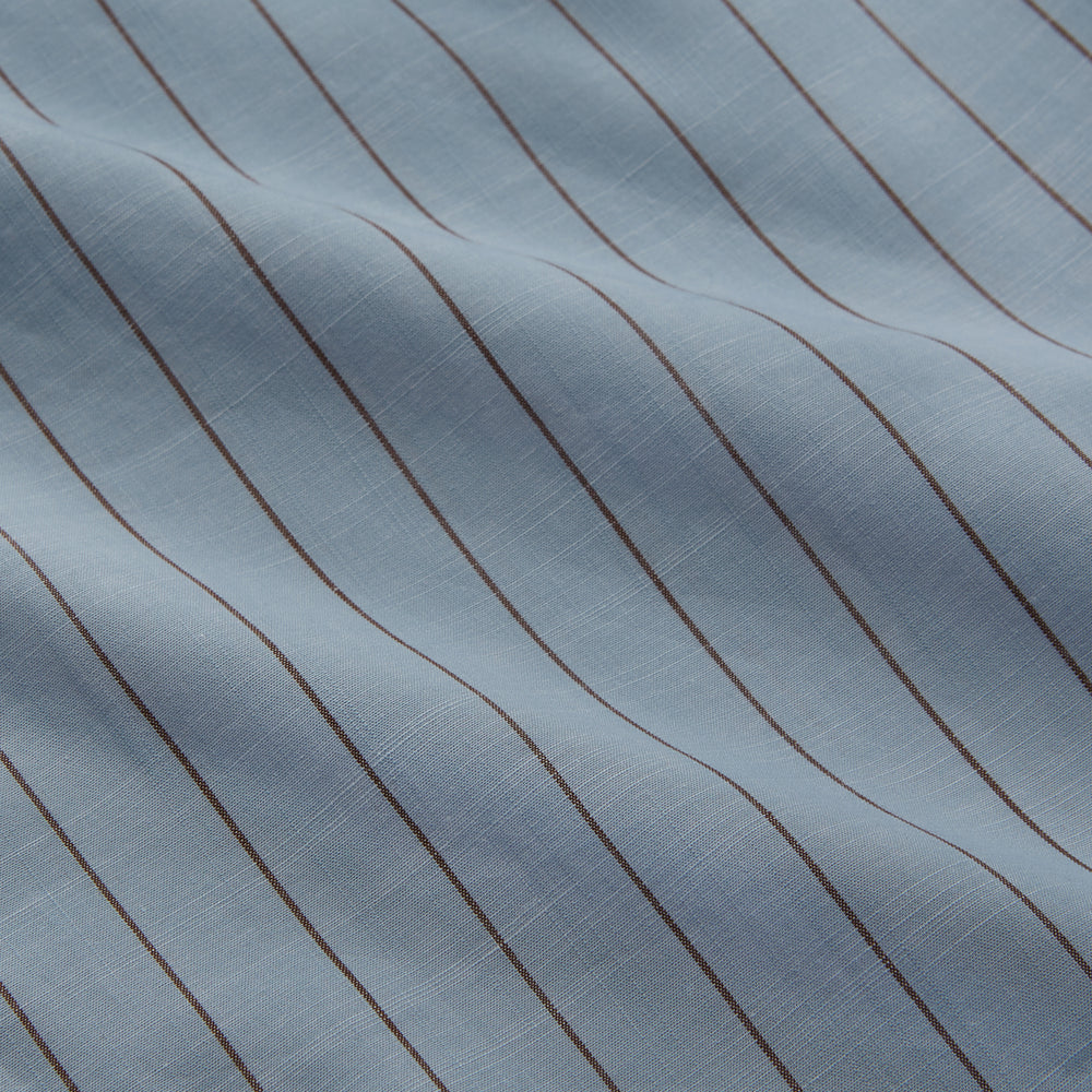 Turnbull & Asser's Pale Blue Stripe Cotton Holiday Fit Shirt features a revere collar, thin black pinstripes, single button cuff, chest pocket, and black buttons—crafted from Italian cotton and laid flat on a white background.