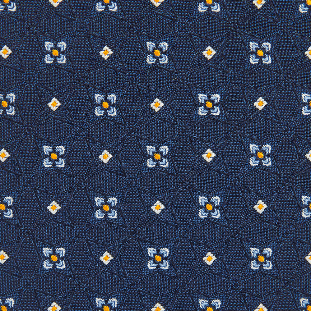 The Turnbull & Asser Navy Floral Emblem Tie displays a repeating pattern of small light blue, white, and yellow floral and diamond motifs, highlighting refined elegance, shown rolled up on a white background.