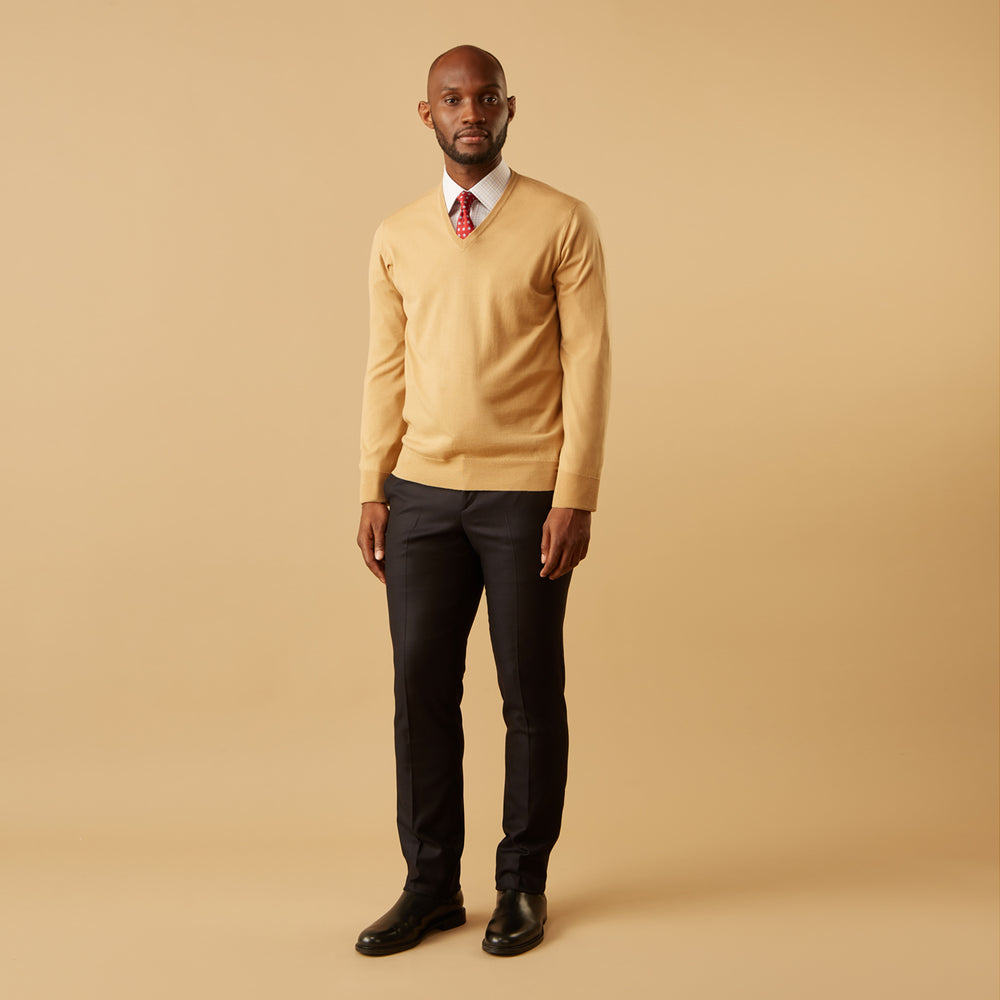 The Turnbull & Asser Camel V-Neck Merino Wool Jumper, with ribbed cuffs and a visible white neckline label, is neatly folded with one sleeve showing—an essential, versatile staple for any gentleman's wardrobe.