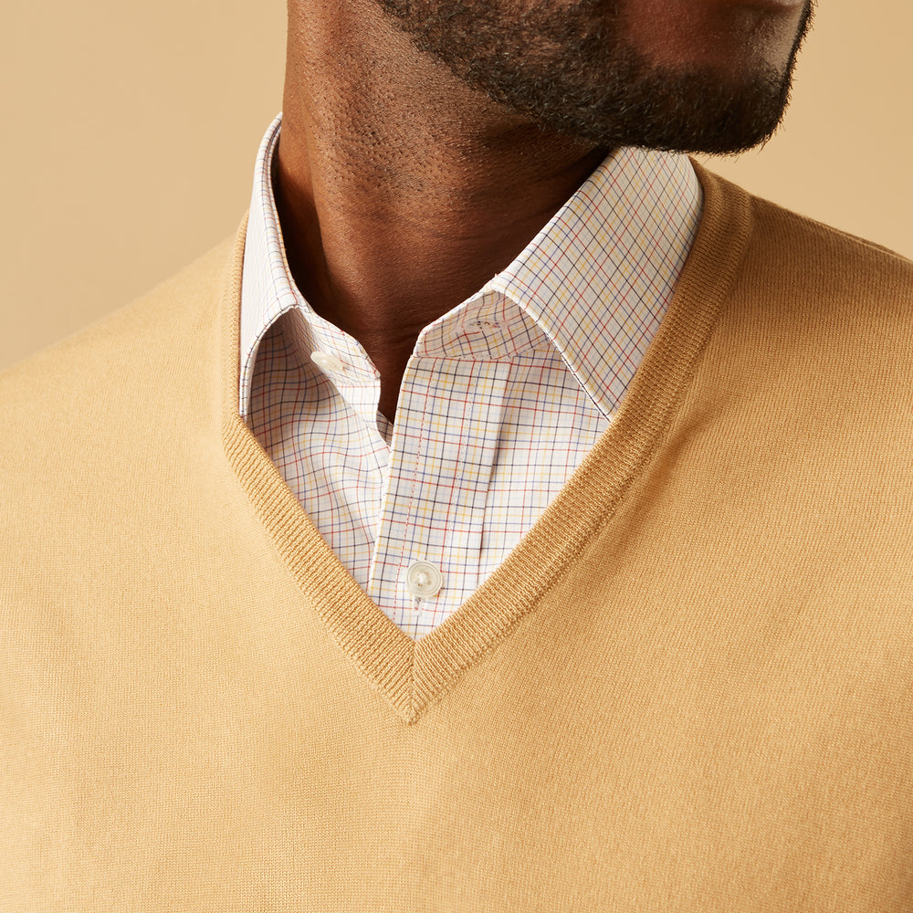 The Turnbull & Asser Camel V-Neck Merino Wool Jumper, with ribbed cuffs and a visible white neckline label, is neatly folded with one sleeve showing—an essential, versatile staple for any gentleman's wardrobe.