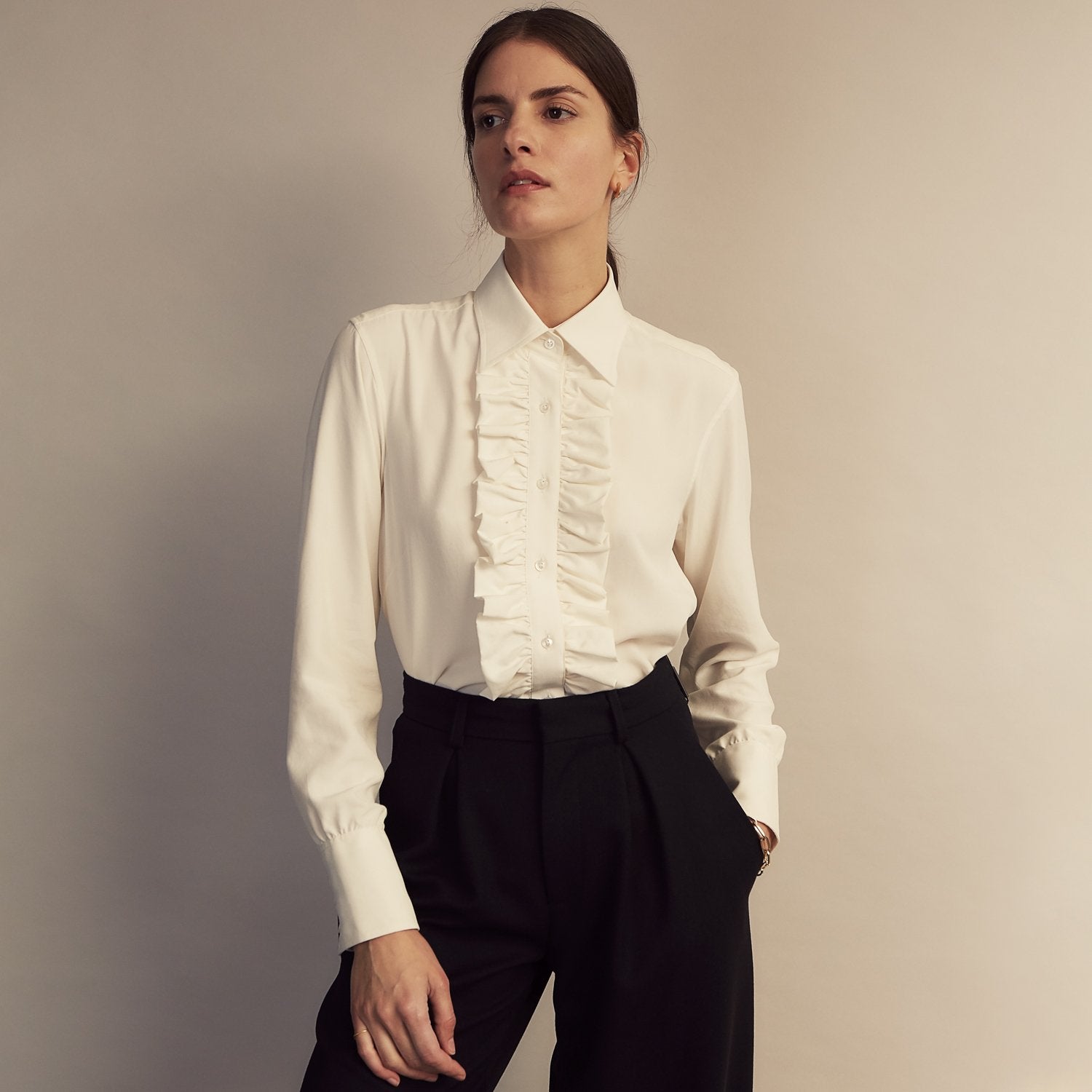 View 7 of product The Turnbull & Asser Turnbull and The Deck Cream Silk Romantic Shirt features long sleeves, a pointed collar, and elegant front ruffles, shown against a plain light gray background.