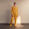 View 1 of product The Turnbull & Asser Women's Gold Silk Harriet Pyjamas Set features a mustard yellow long-sleeve, button-up top with revere collar and chest pocket, plus matching drawstring pants with an elasticated waist, displayed on a white background.