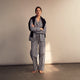 A person stands barefoot on a gray floor in the Turnbull & Asser Blue Multi Stripe Harriet Women’s Pyjama Set with a dark sweater over their shoulders—premium cotton pyjamas that make a perfect gift for her—against a plain beige background.