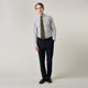 A man stands against a light background, wearing a Turnbull & Asser Yellow and Blue Fancy Check Regular Fit Shirt with T&A Collar, a patterned tie, dark dress pants, and black shoes. He faces forward with hands in pockets and a neutral expression.