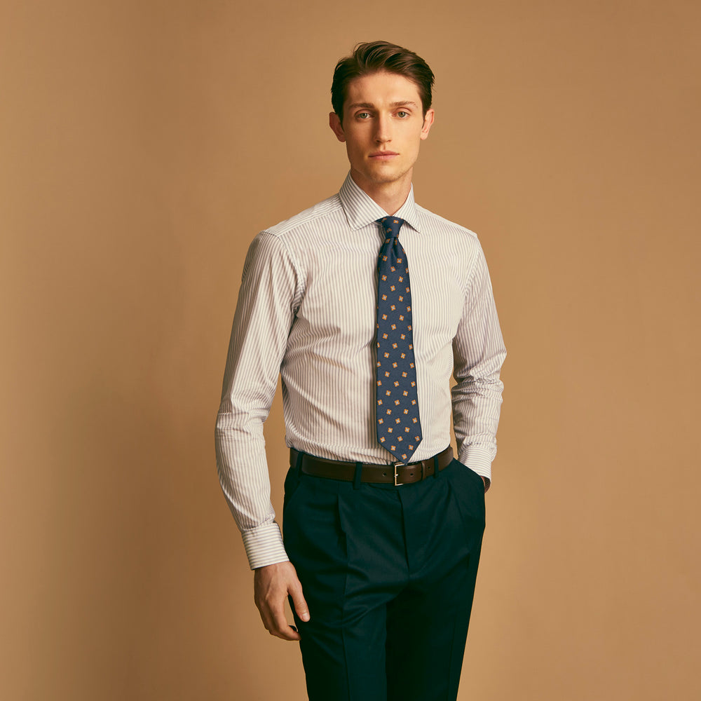 A man wearing the Turnbull & Asser Grey Multi Stripe Regular Fit Twill Shirt with T&A Collar and Double Cuffs stands against a beige background, one hand in his pocket, looking at the camera.